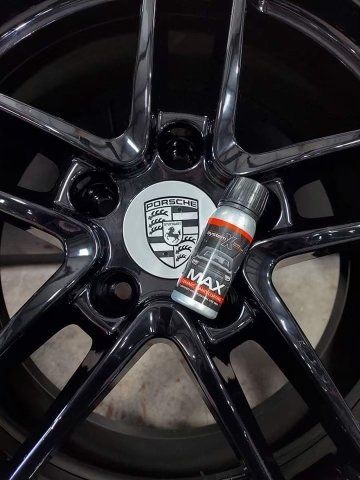 Black Porsche wheel with crest center cap and a small red-and-silver bottle resting on the rim