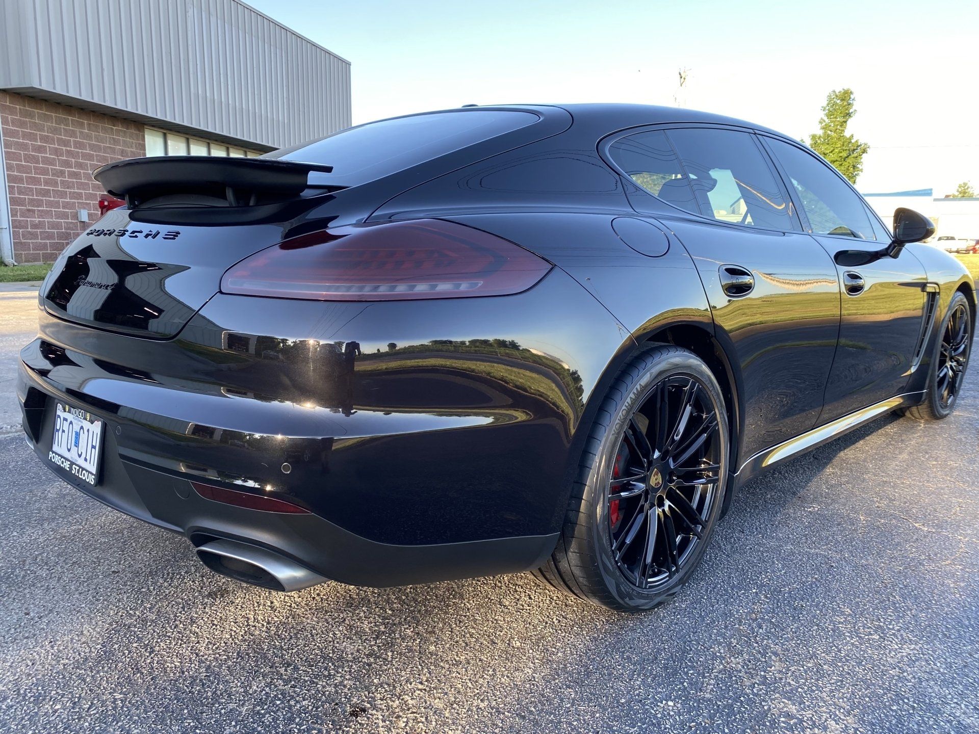 Black sports car parked outdoors on gravel beside a building, shown from the rear side.