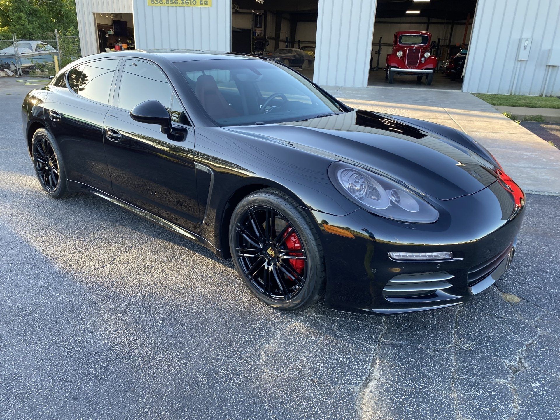 Black Porsche sedan parked outside a garage, with black wheels and red brake calipers.