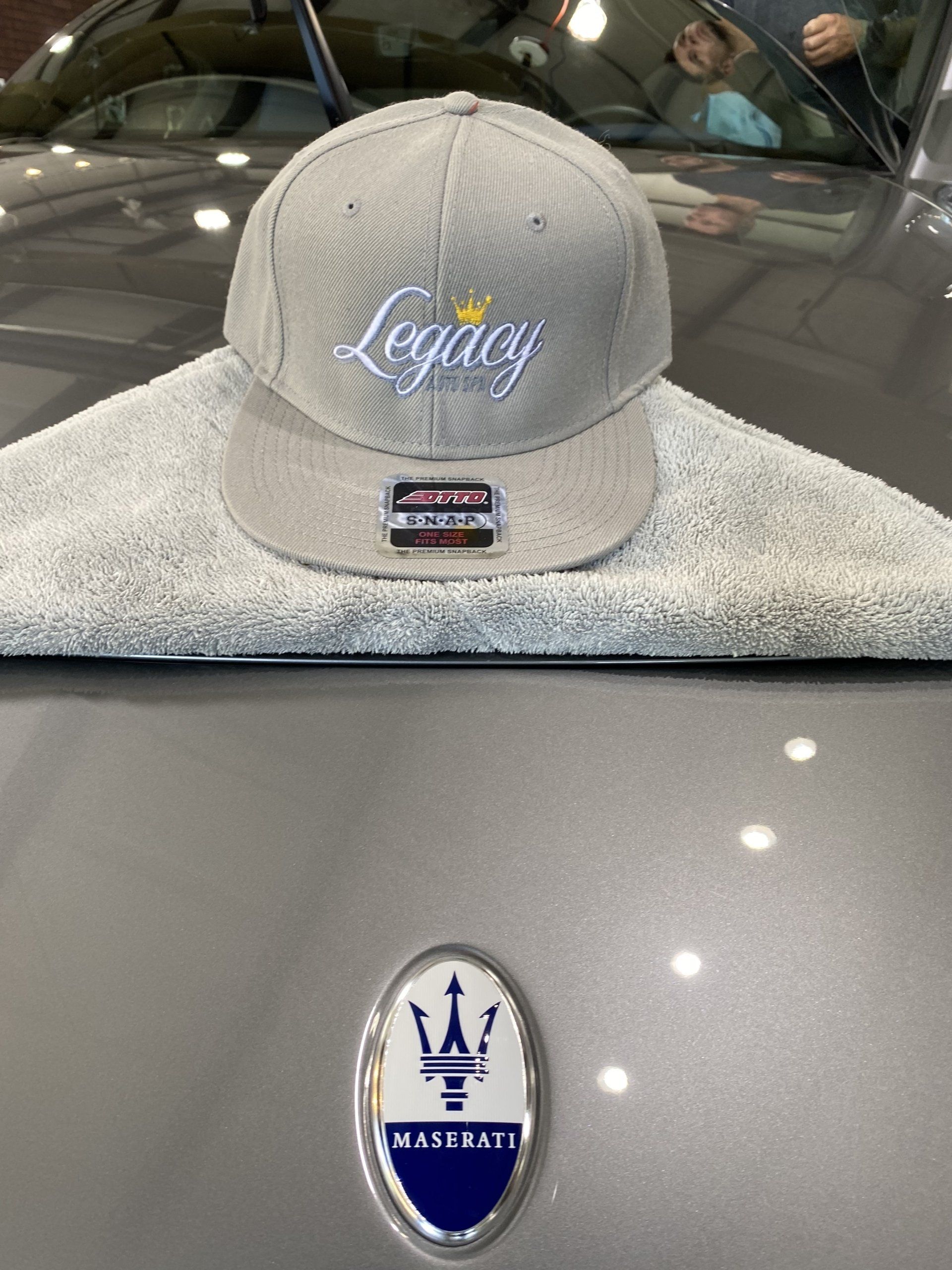 Gray Maserati hood with logo and a gray “Legacy” cap resting on it inside a car showroom