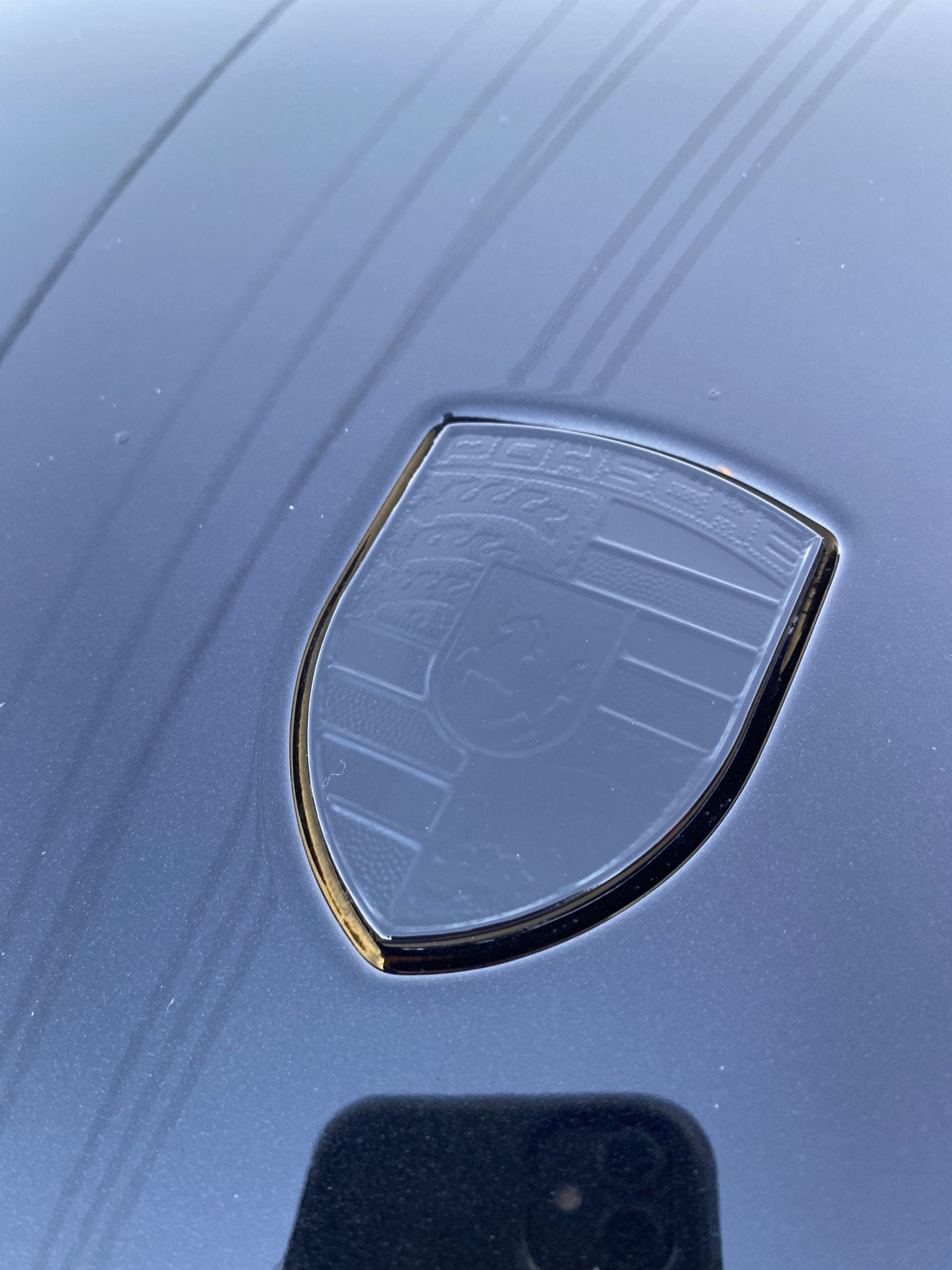 Close-up of a black car hood badge with scratches on a blue surface