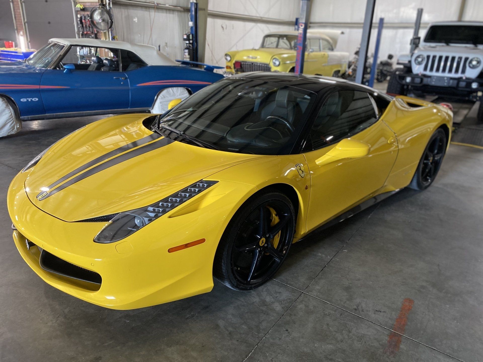 Yellow sports car parked indoors in a garage, with classic cars in the background