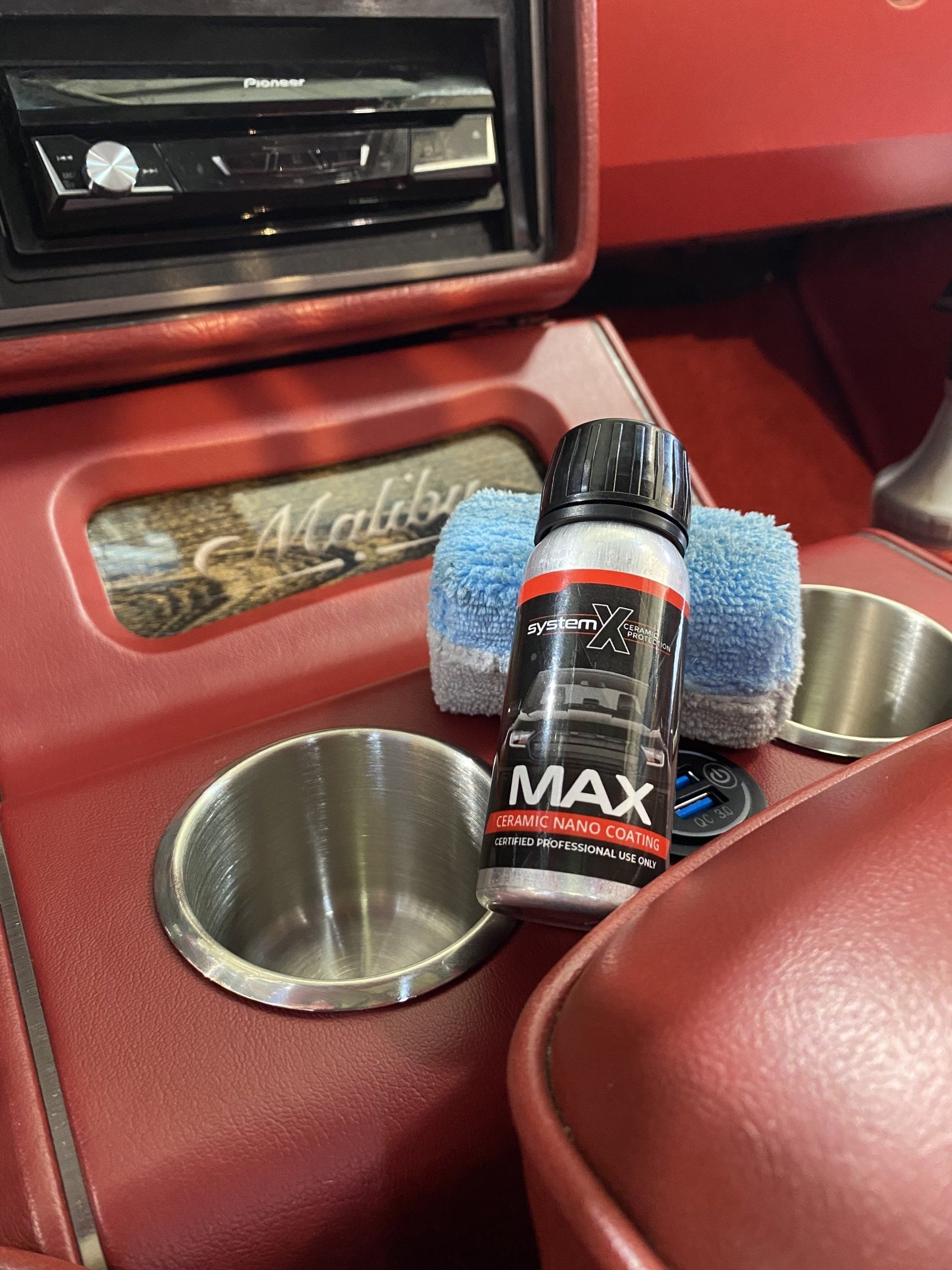 Car interior cup holder with a MAX spray can and cleaning cloth on a red console