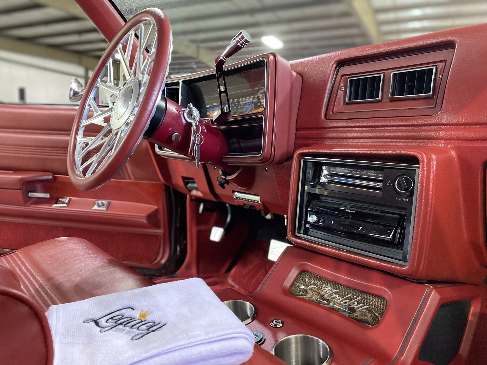Red classic car interior with white steering wheel, dashboard, and folded white cloth on the seat