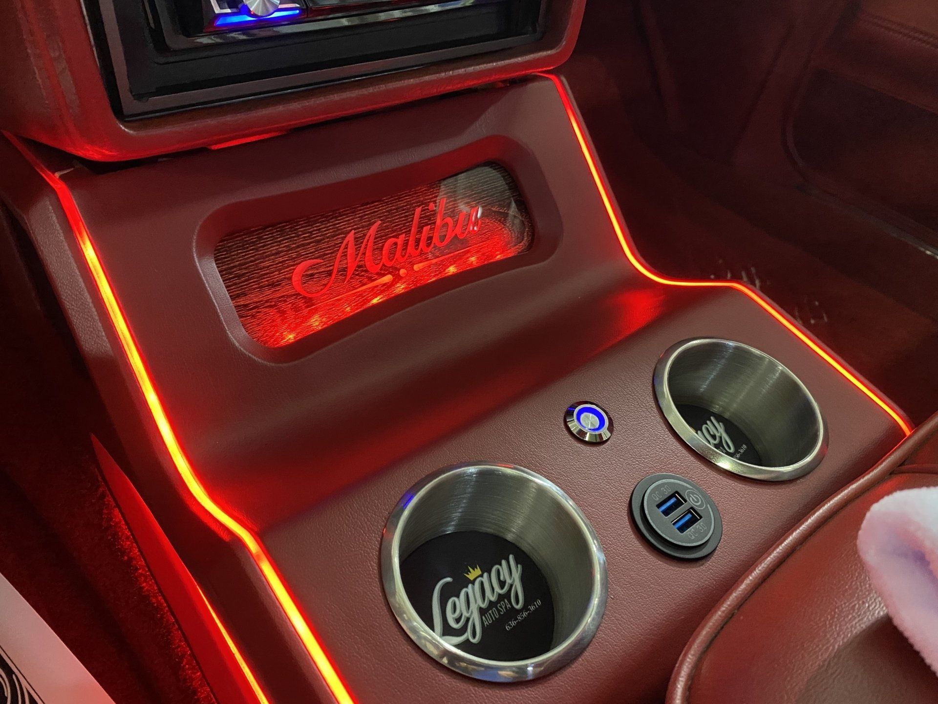 Red-lit car console with two cup holders and illuminated buttons, seen from the passenger side