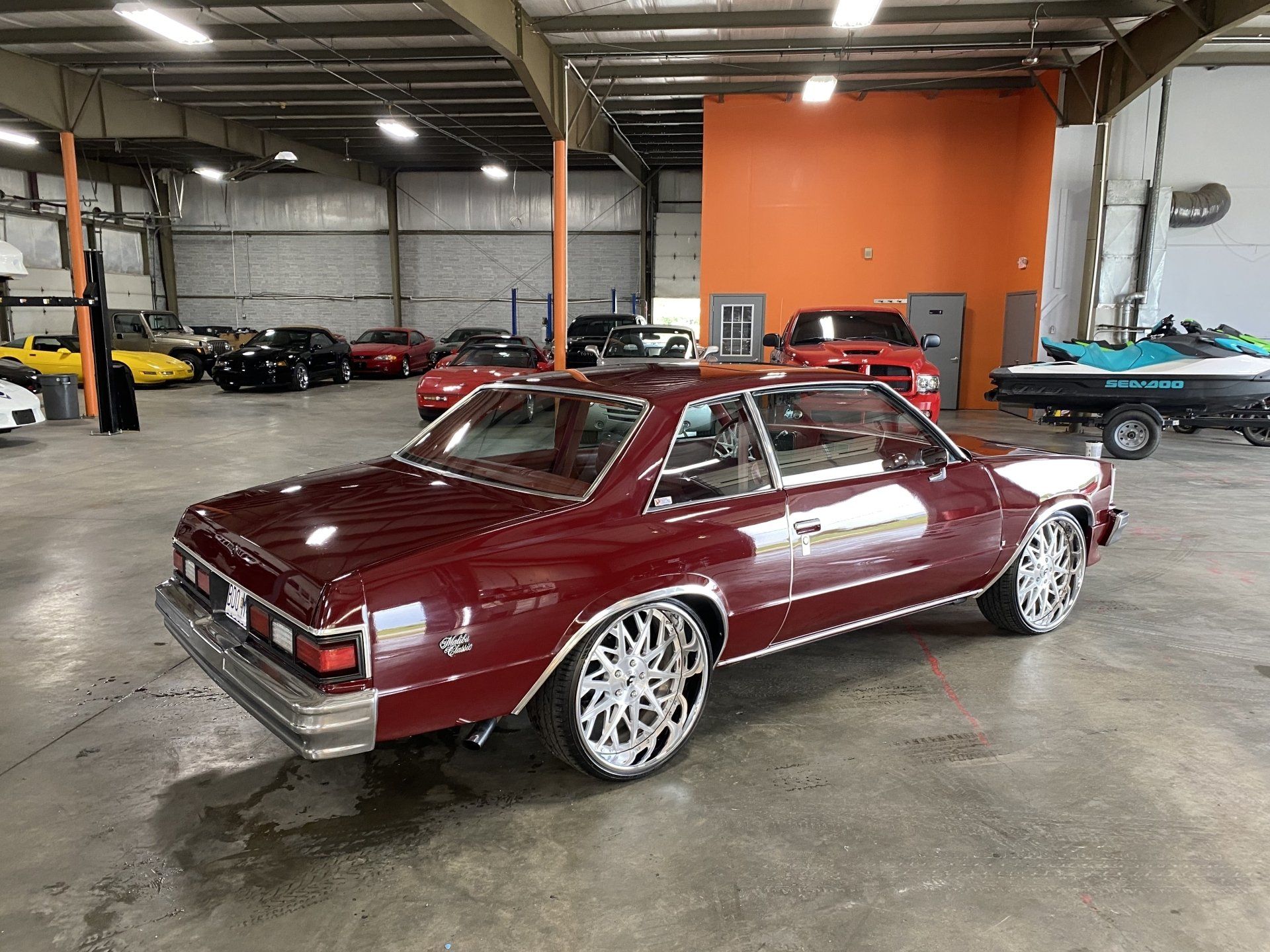Maroon classic coupe with chrome wheels in an indoor garage showroom