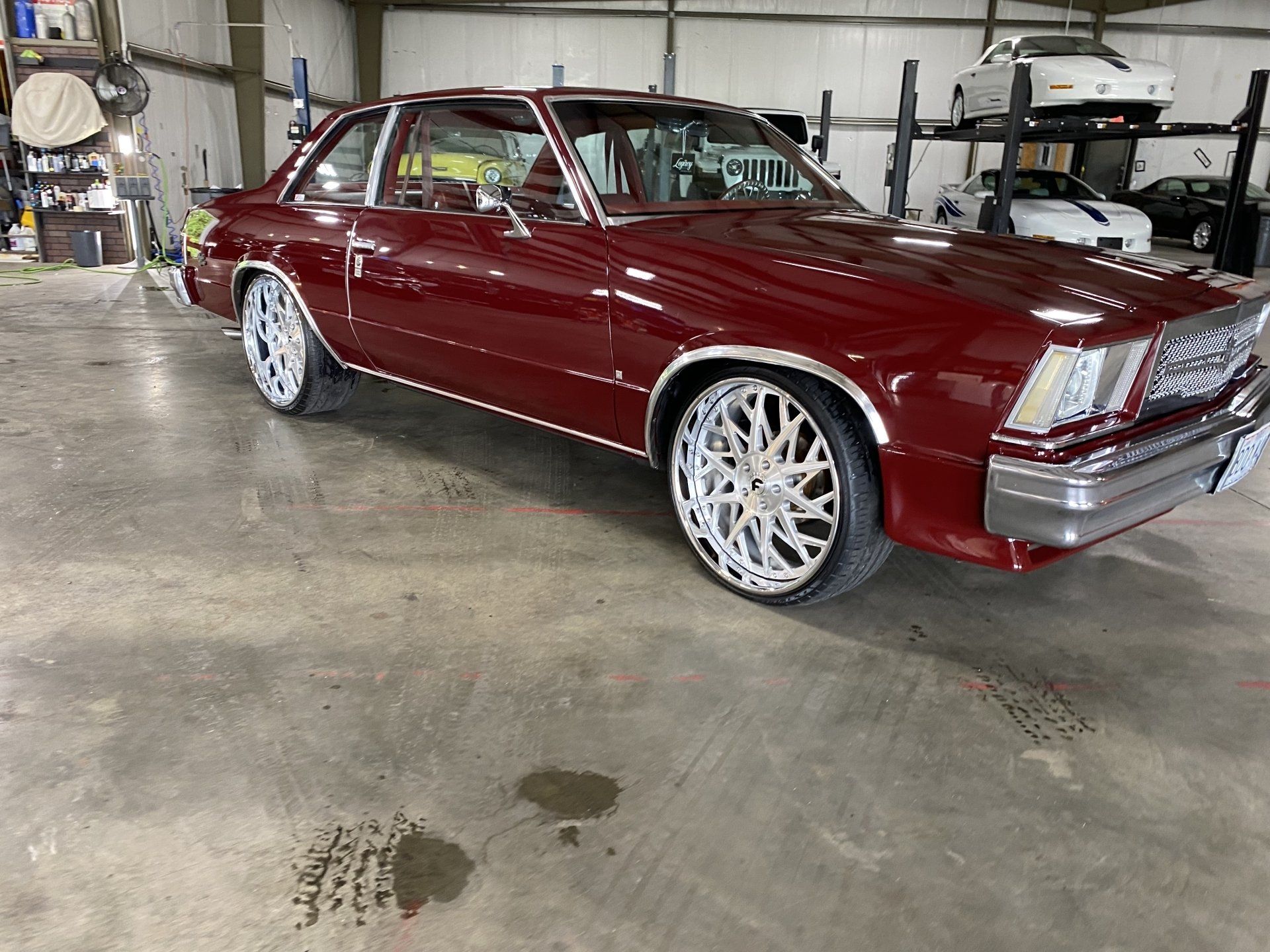 Maroon classic sedan with chrome wheels parked in a garage workshop