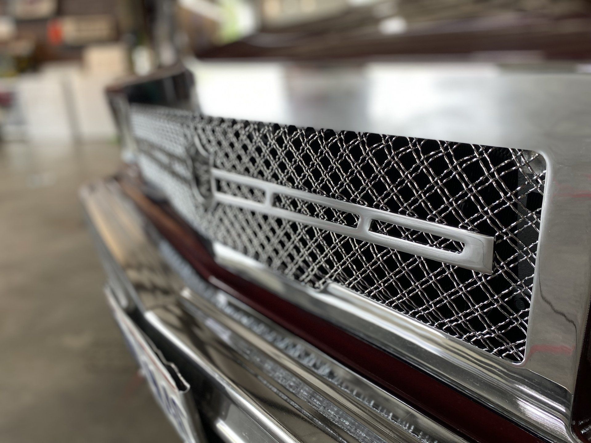 Close-up of a chrome car grille with diamond mesh and a red accent line.