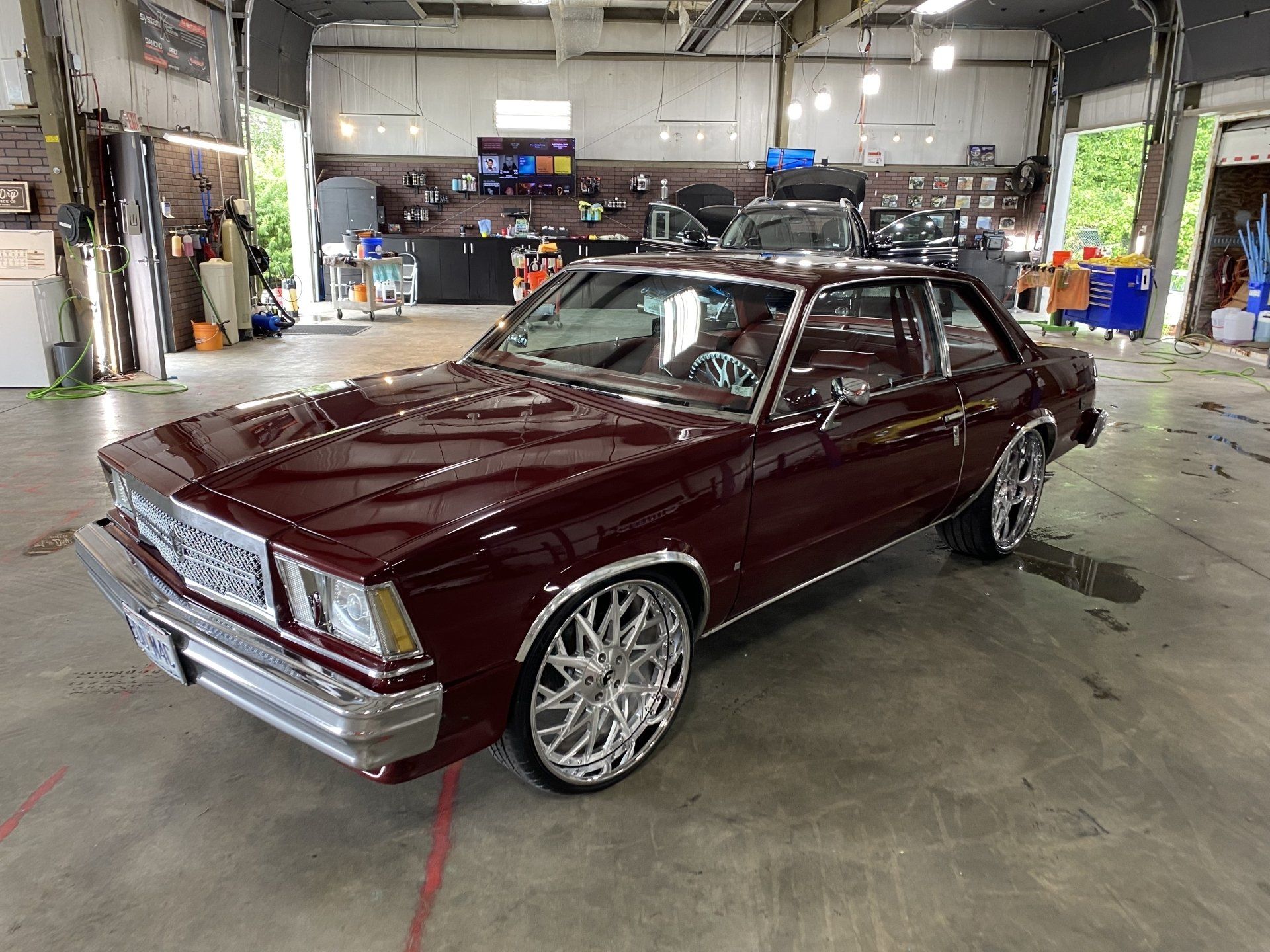 Maroon classic coupe with chrome trim parked in an auto shop garage