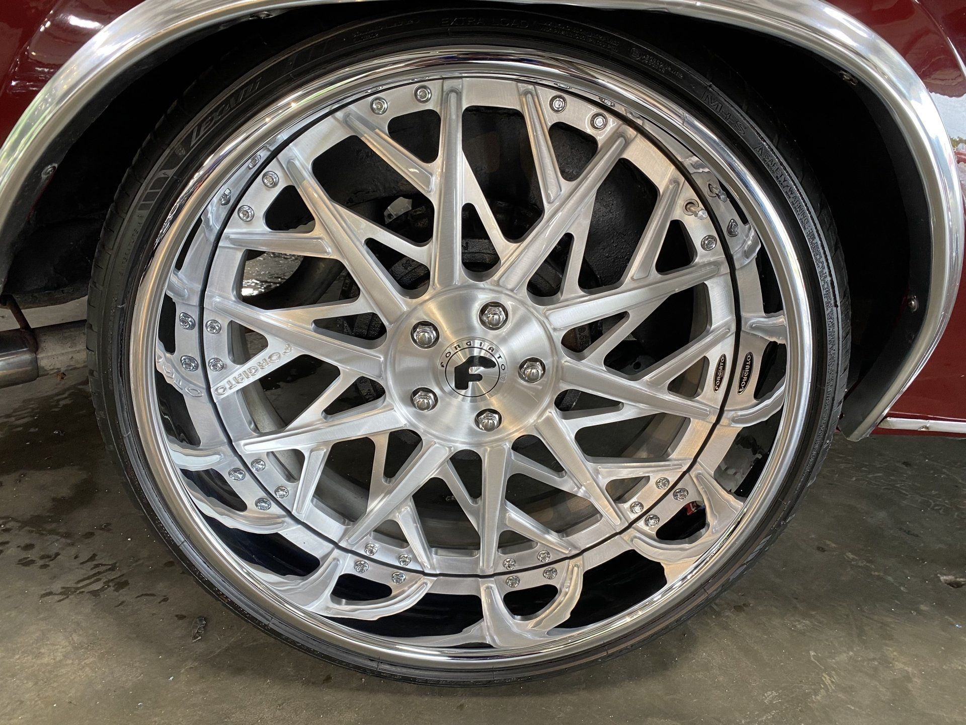 Close-up of a silver multi-spoke car wheel rim with low-profile tire in a garage