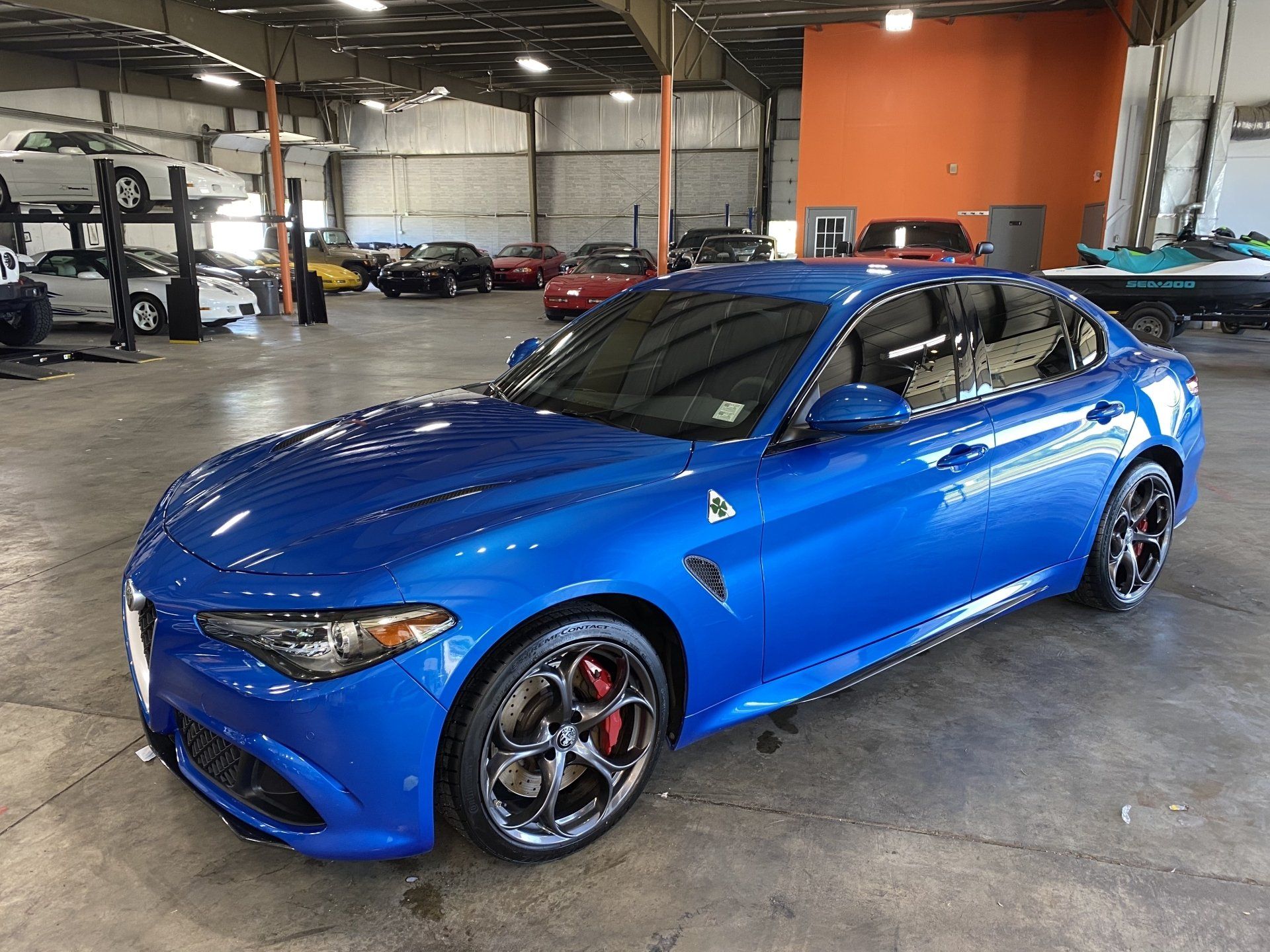 Blue sports sedan in an auto shop garage, viewed from the front-left side.
