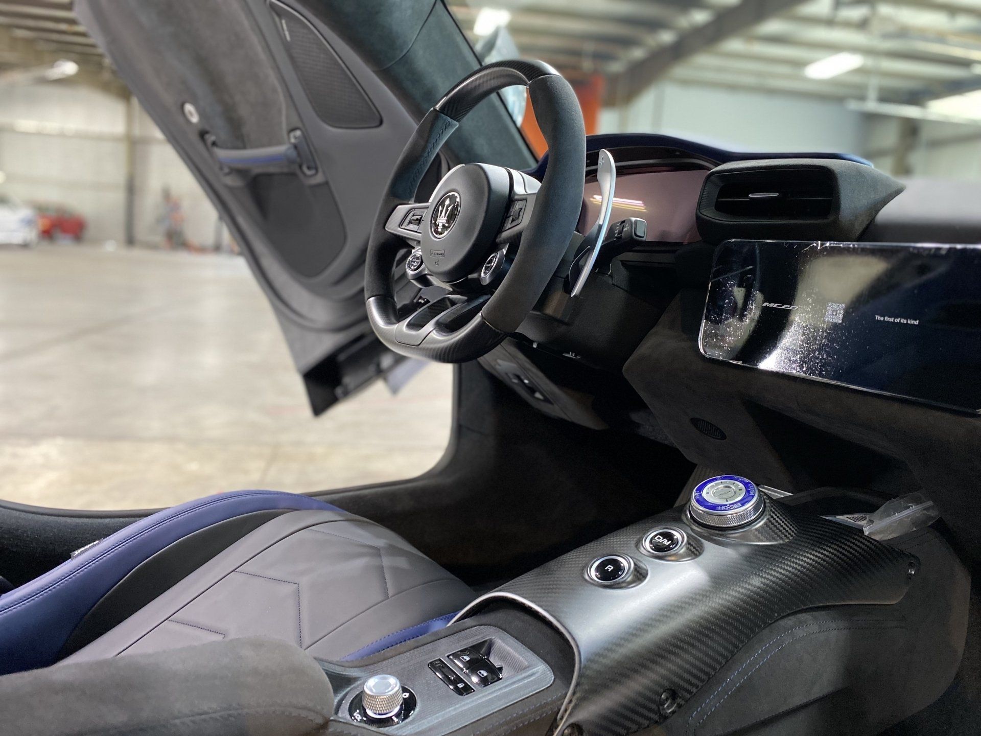 Luxury sports car interior with carbon fiber center console, steering wheel, and open door in a garage