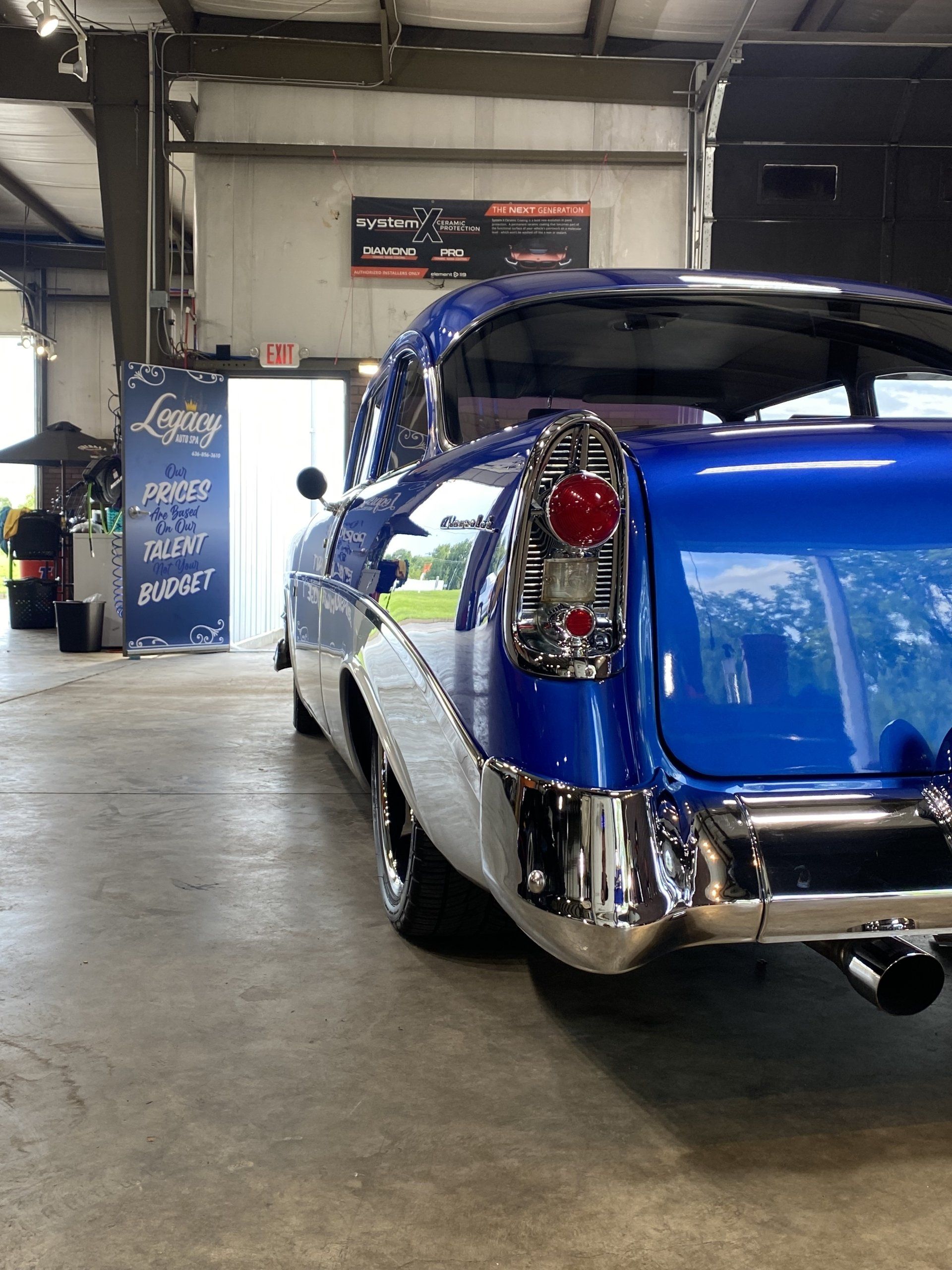 Blue classic car in a garage, rear view with chrome details and red taillights.