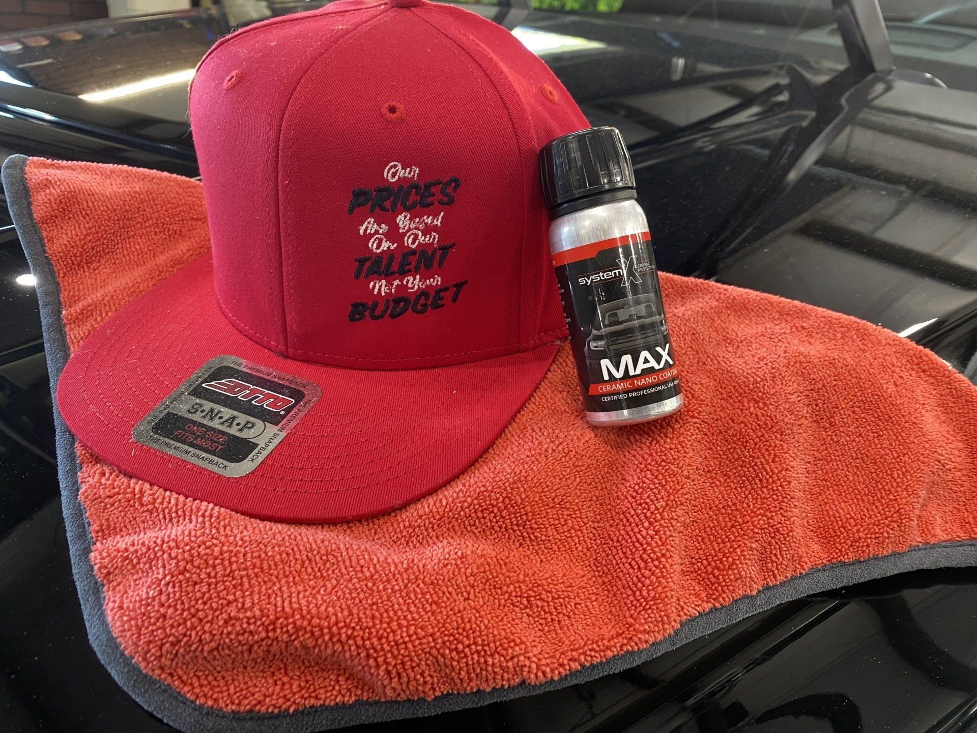 Red cap and small bottle on an orange towel draped over a car hood.