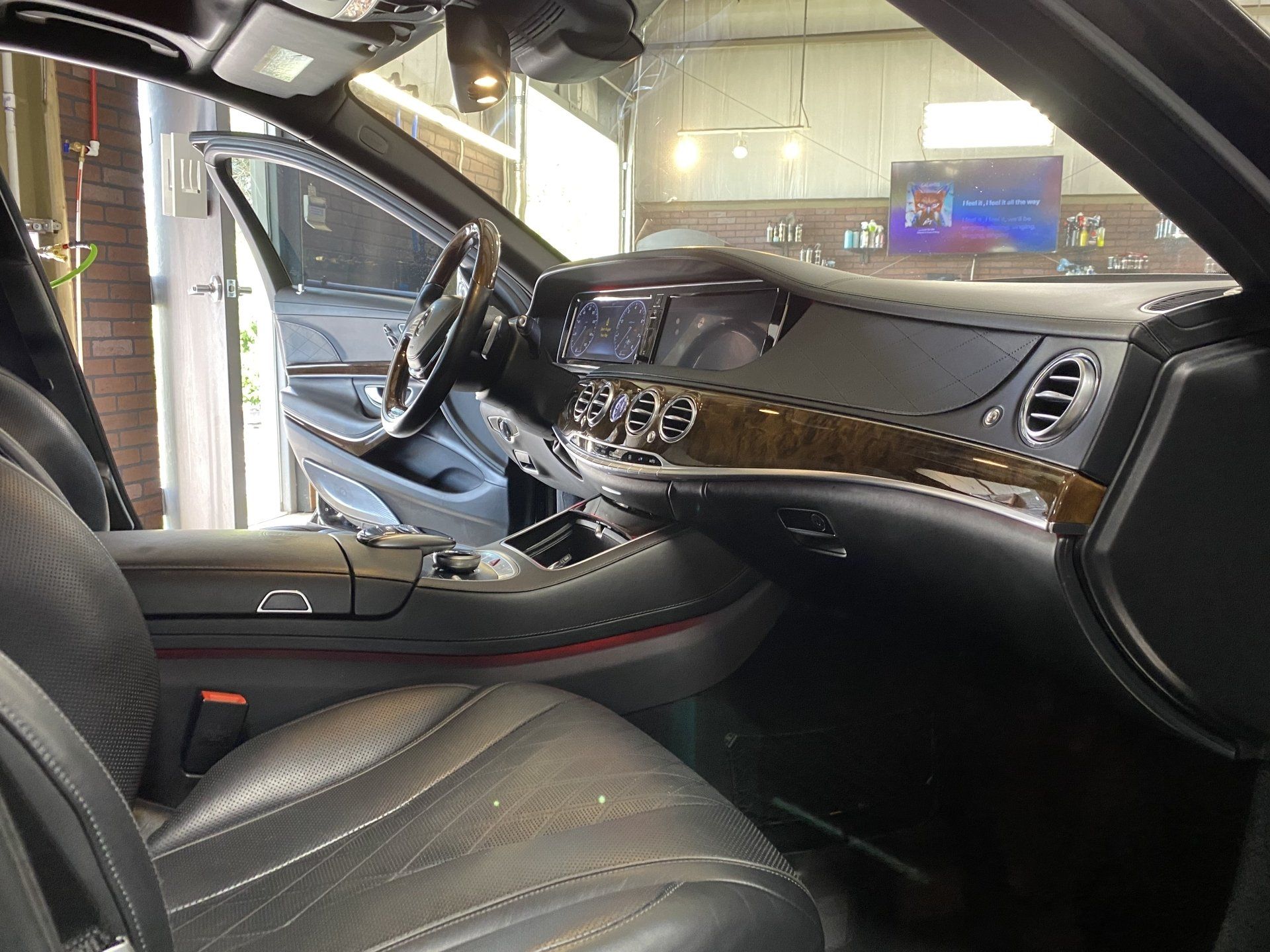Luxury car interior with black leather seats, wood trim dashboard, and open driver door in a garage