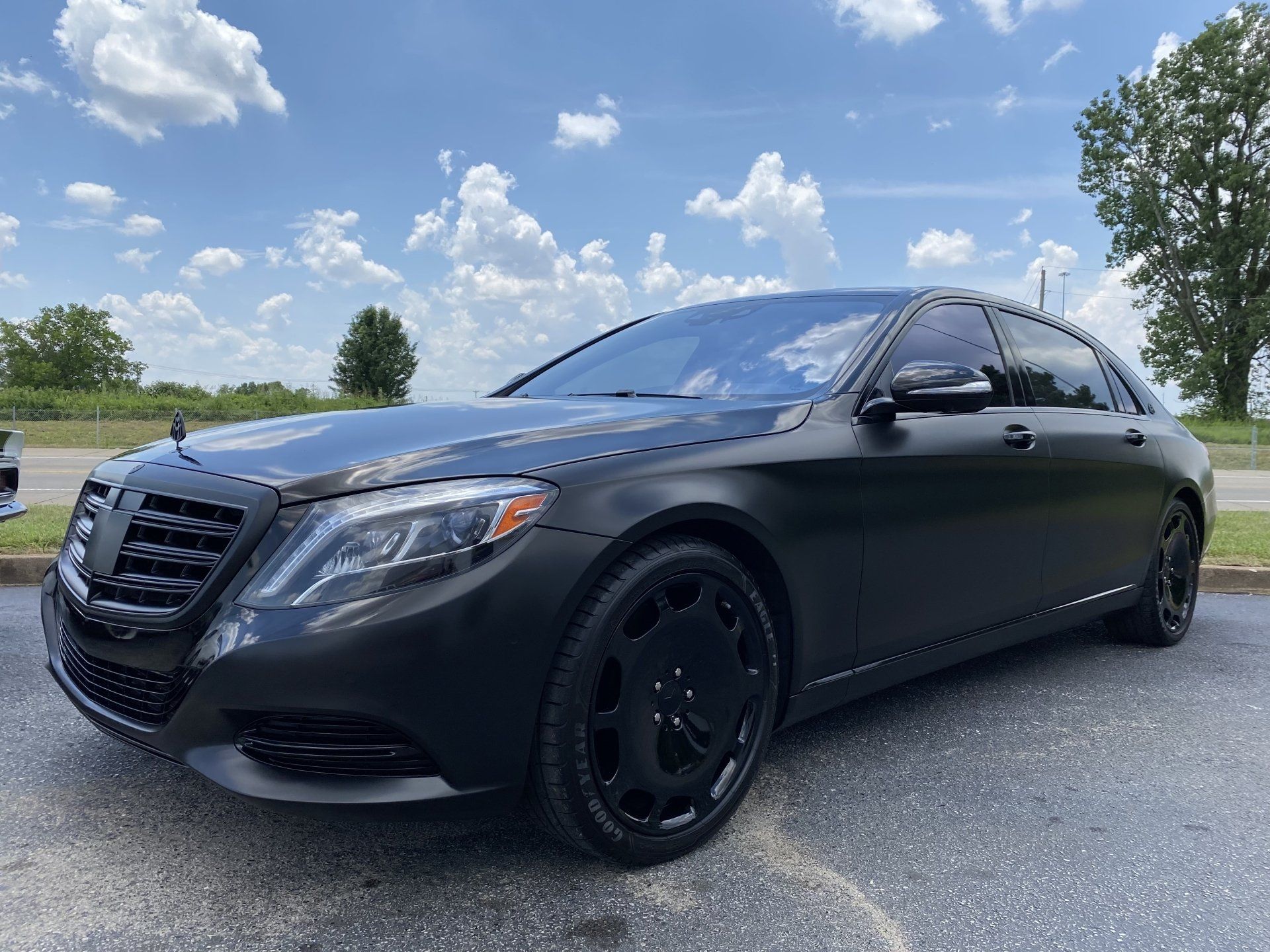 Black sedan parked on gravel under a blue sky with clouds, seen from the front-left side.