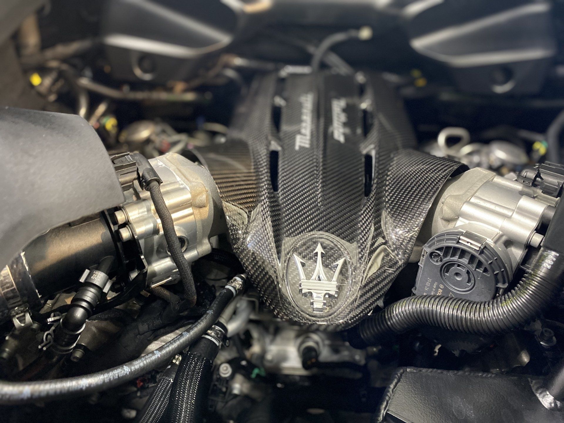 Close-up of a Maserati engine bay with carbon-fiber cover and twin silver turbochargers