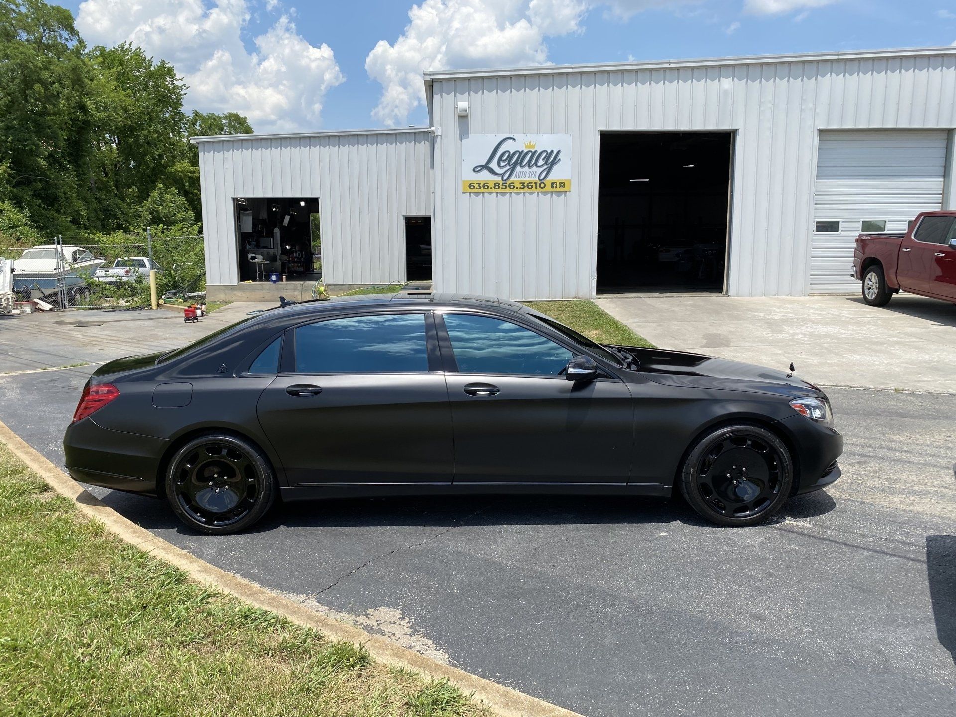 Black sedan parked outside a white auto shop with open garage bays.