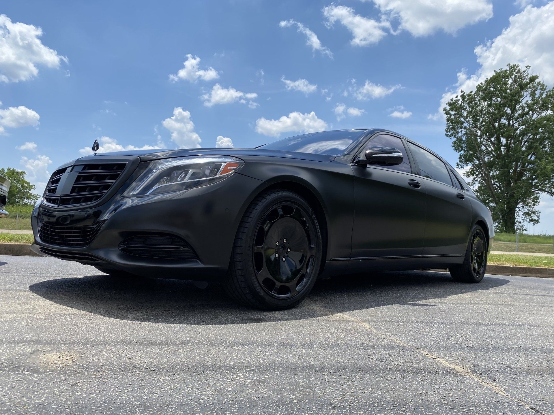 Black sedan parked on a road under a blue sky with clouds and trees nearby