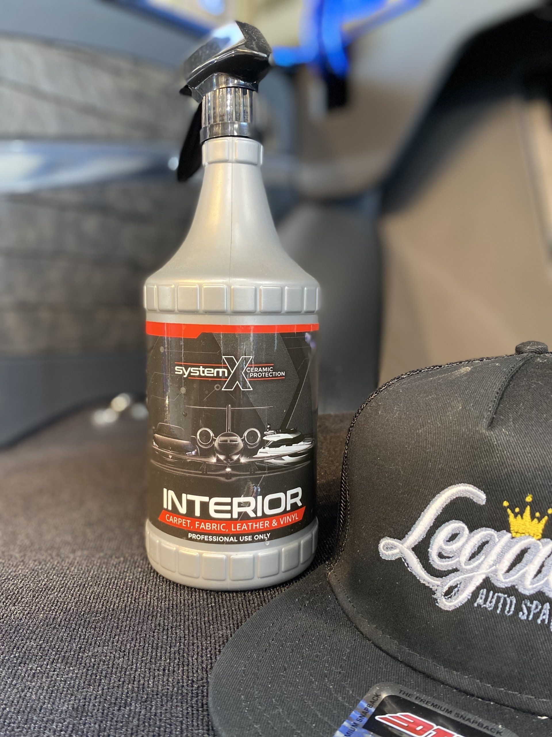 Bottle of interior cleaner on a car seat next to a black cap with white embroidery.