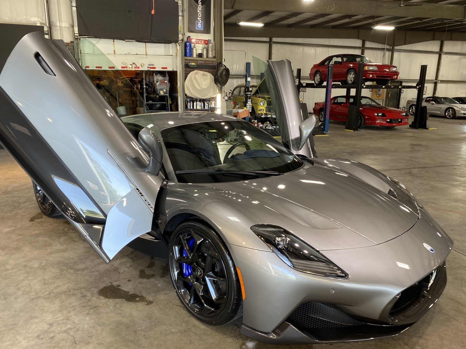 Silver sports car with butterfly doors open in a garage, showing blue brake calipers.
