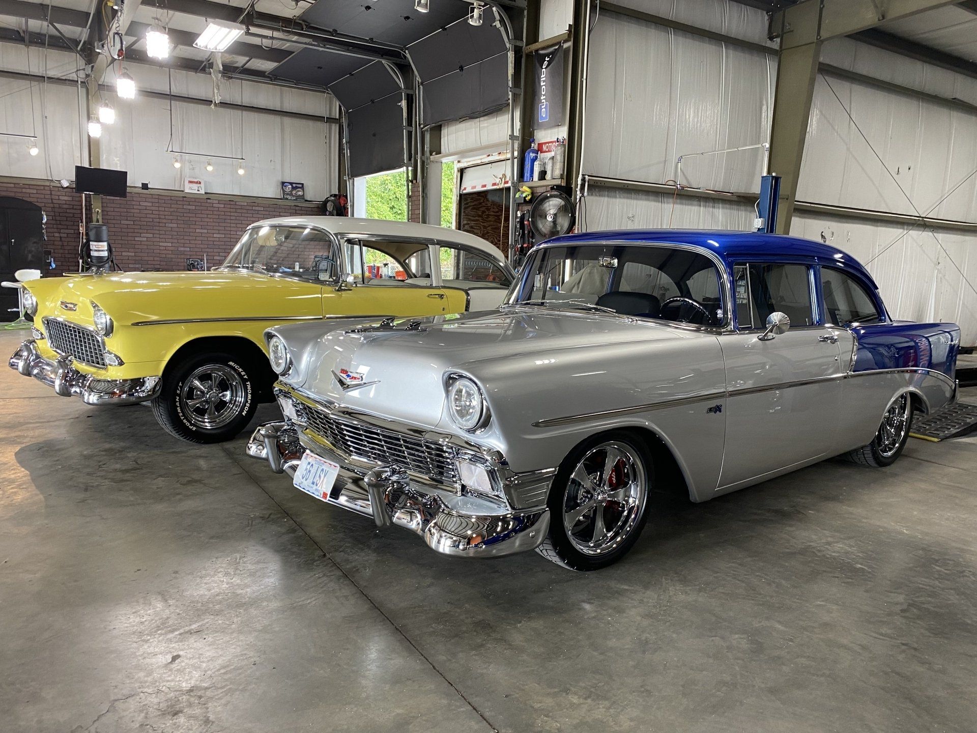 Classic cars in a garage: silver coupe with blue roof and yellow vintage car behind it.