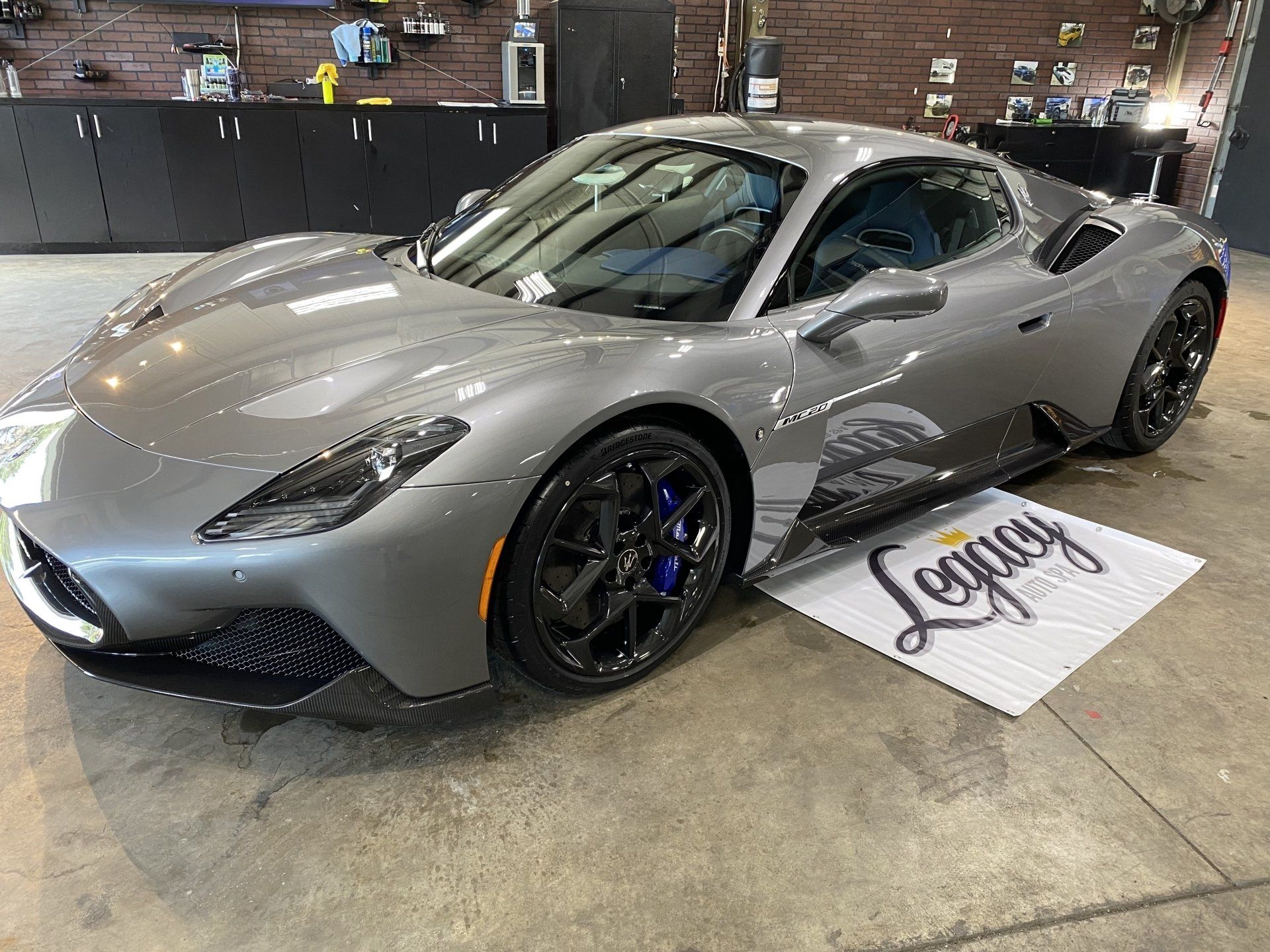 Silver sports car displayed indoors on a showroom floor, with a sign beside it