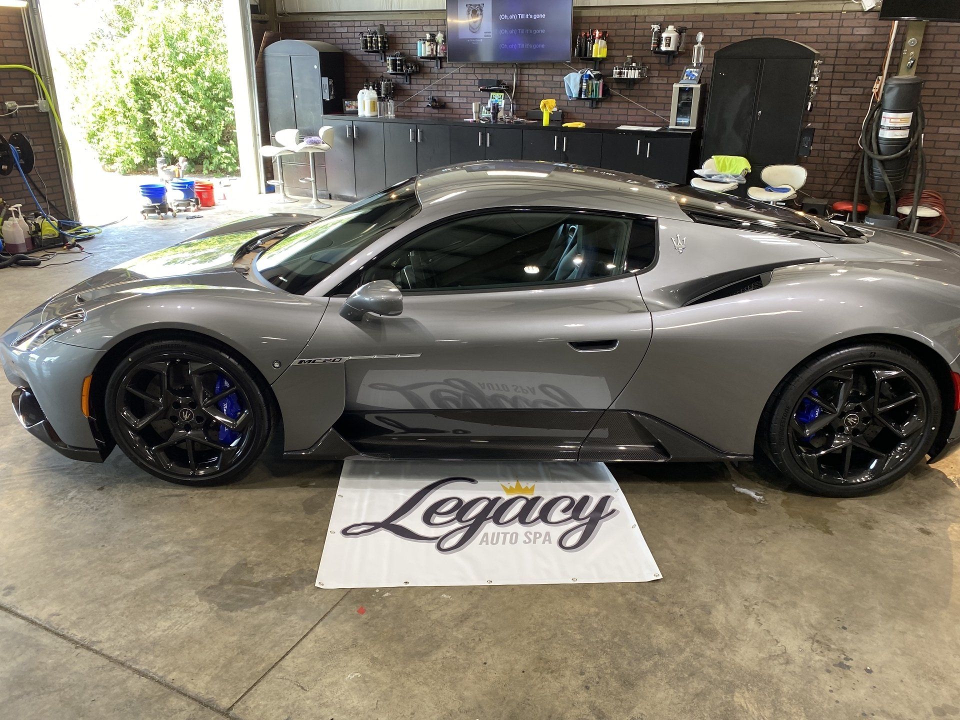 Gray sports car in a garage, parked beside a “Legacy” floor mat.