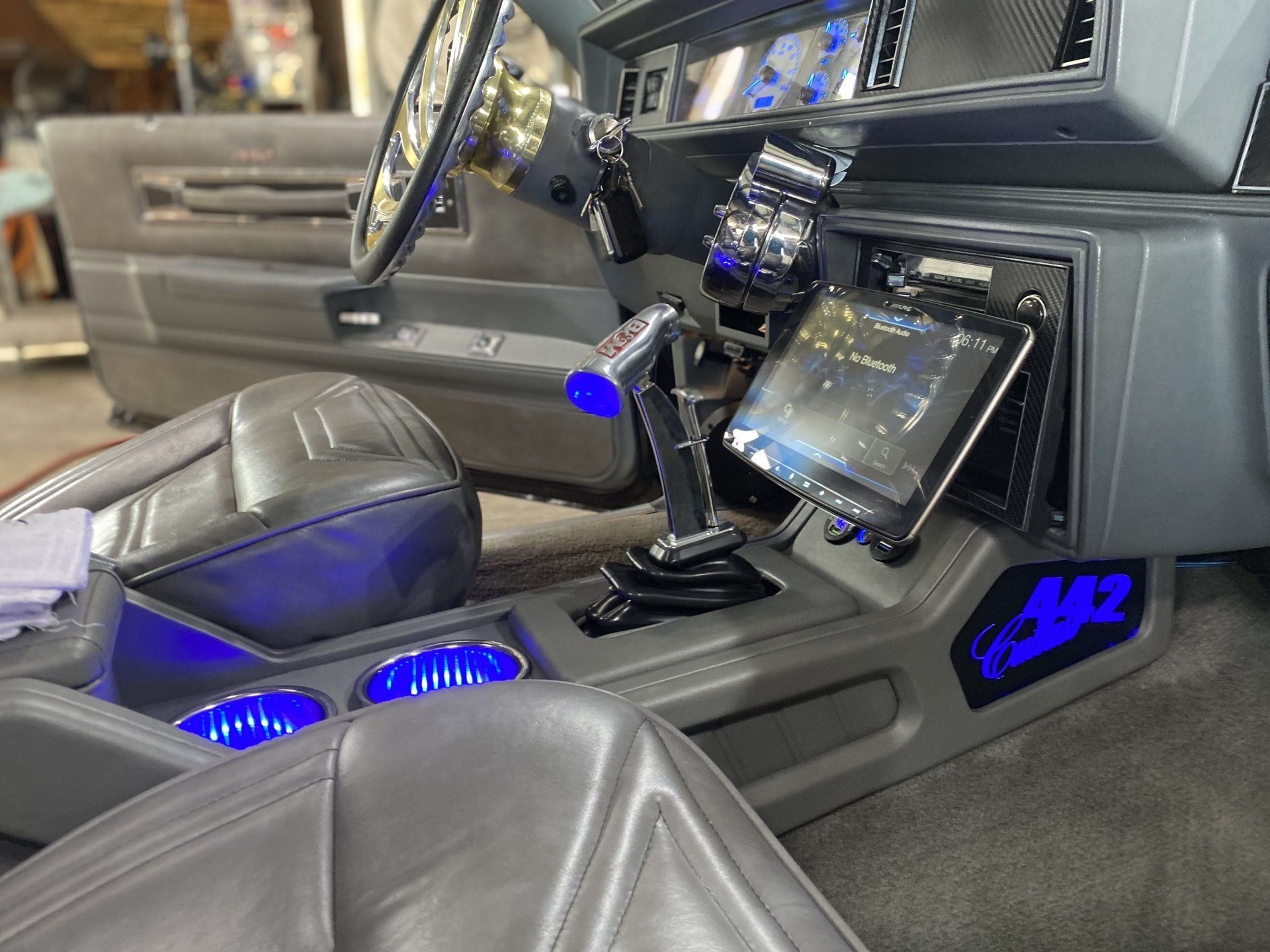 Custom black car interior with blue LED lighting, touchscreen dash, and bucket seats