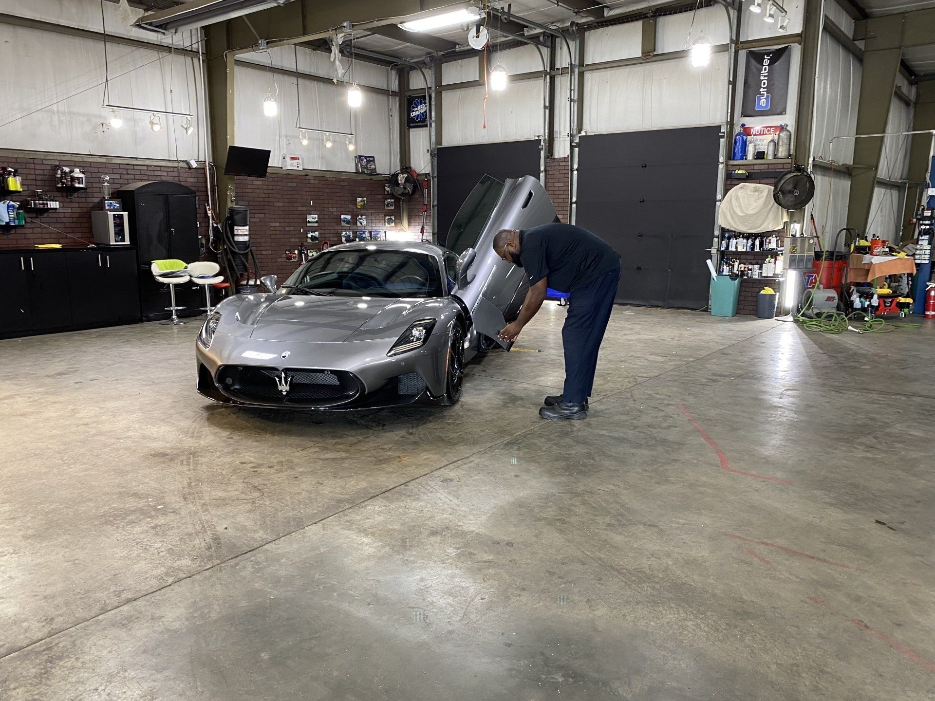 Man bending over a silver sports car in an auto shop garage with the hood open