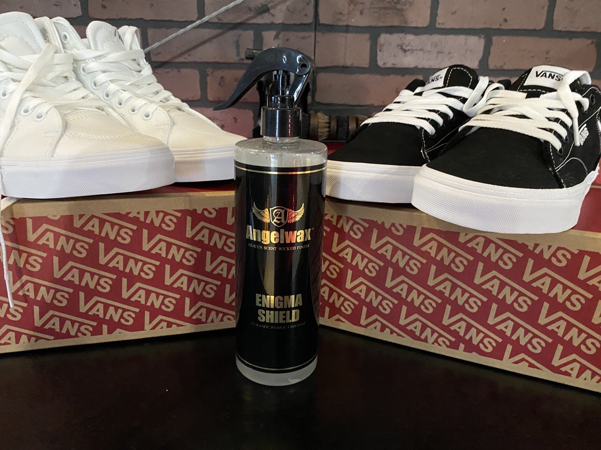 Vans shoes on boxes with a black bottle centered between black and white sneakers against a brick wall