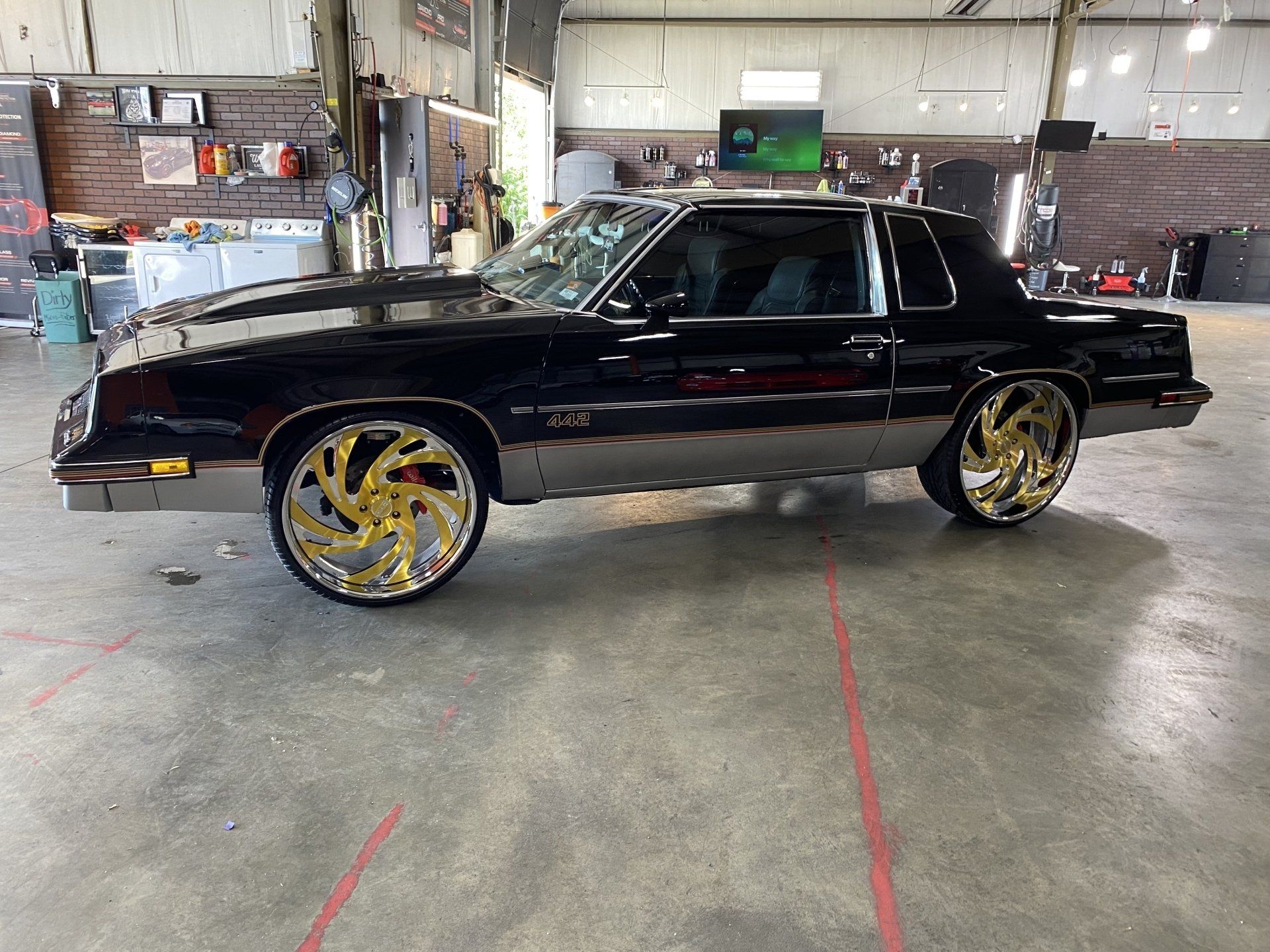 Black classic car with gold rims in an auto shop garage.