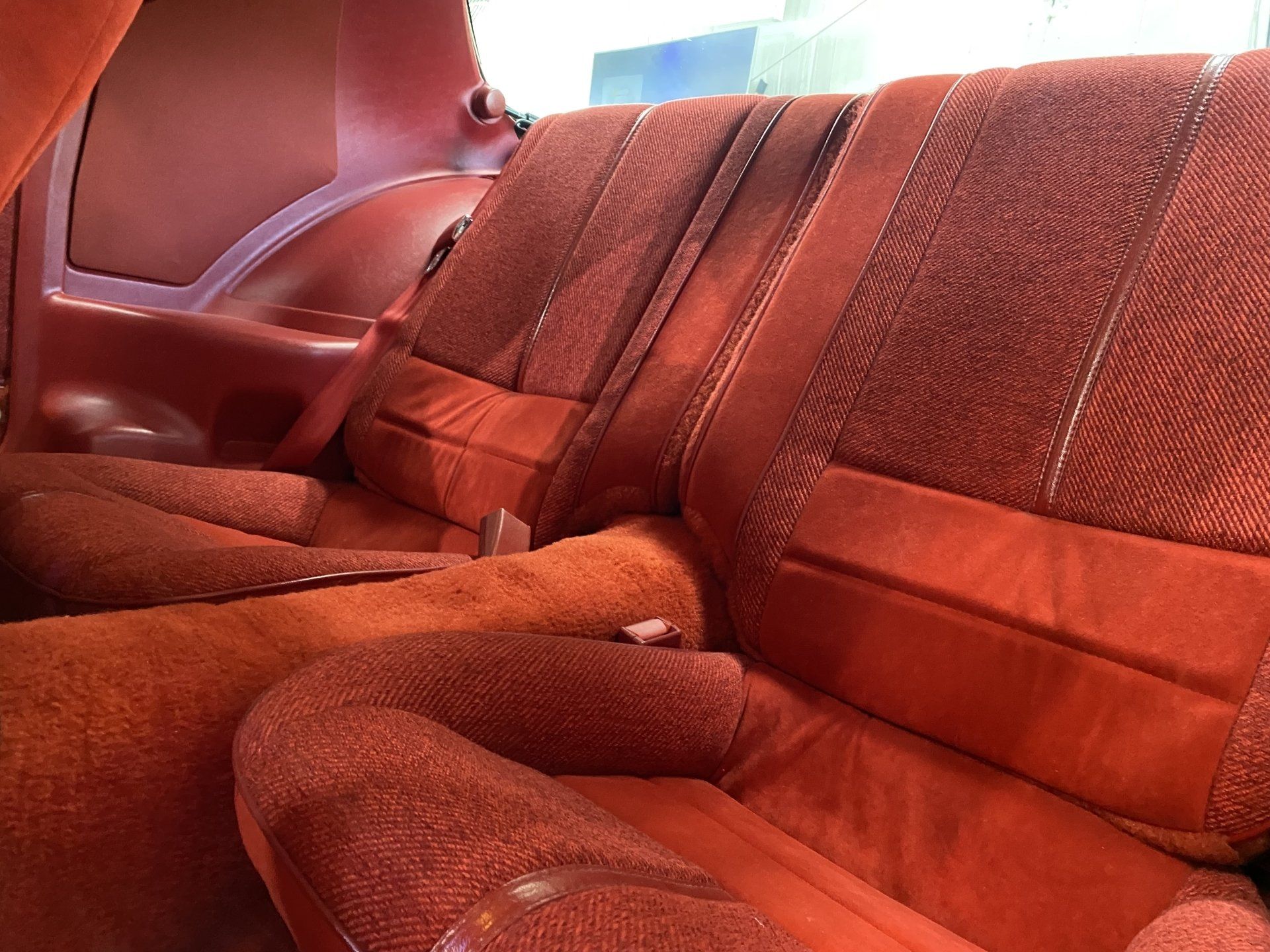 Red car interior with plush red seat covers and folded rear seats, showing the back seat area.