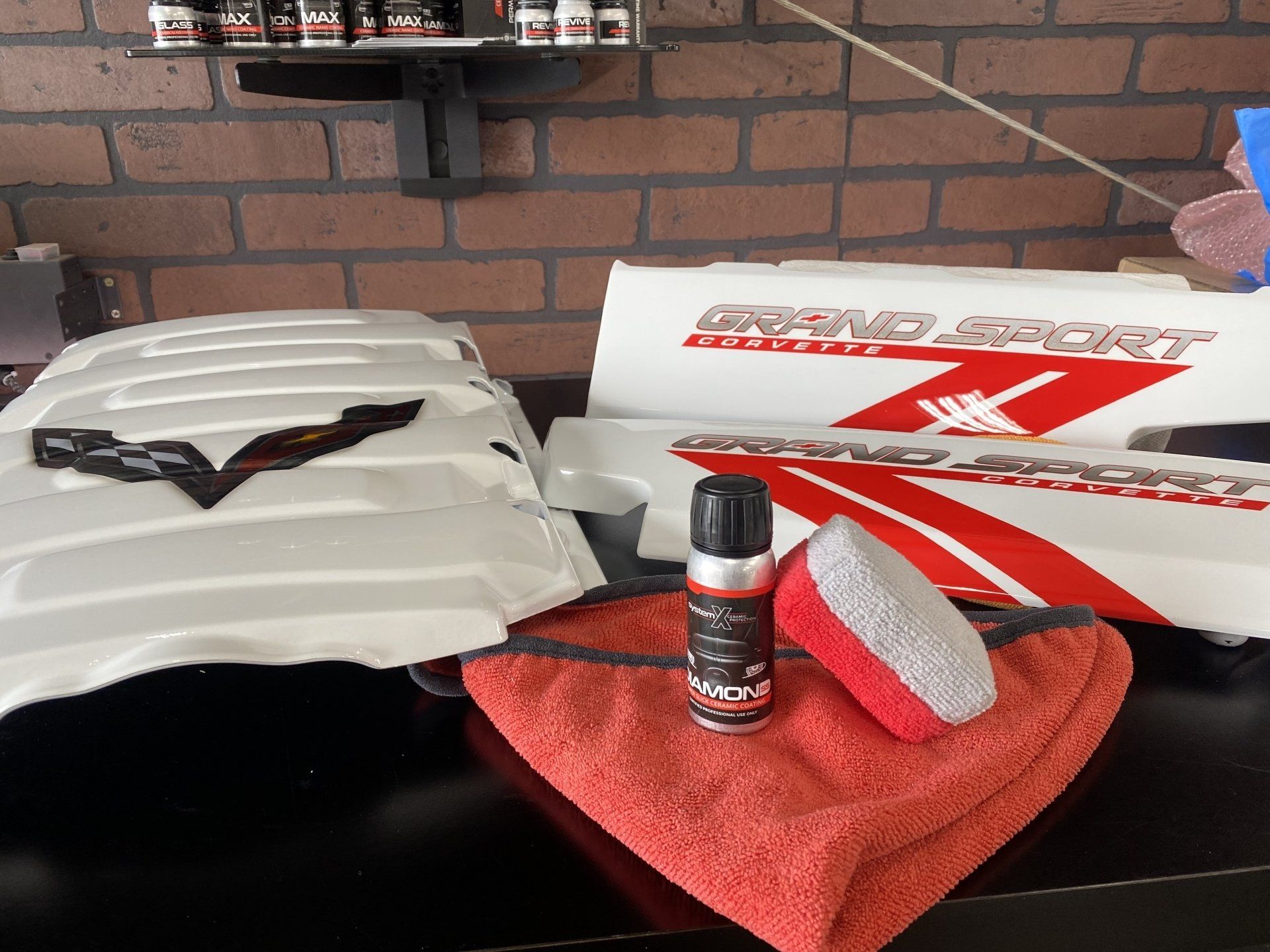 Car-care products and tools on a tabletop, including a red cloth, spray can, sponge, and car hood emblems