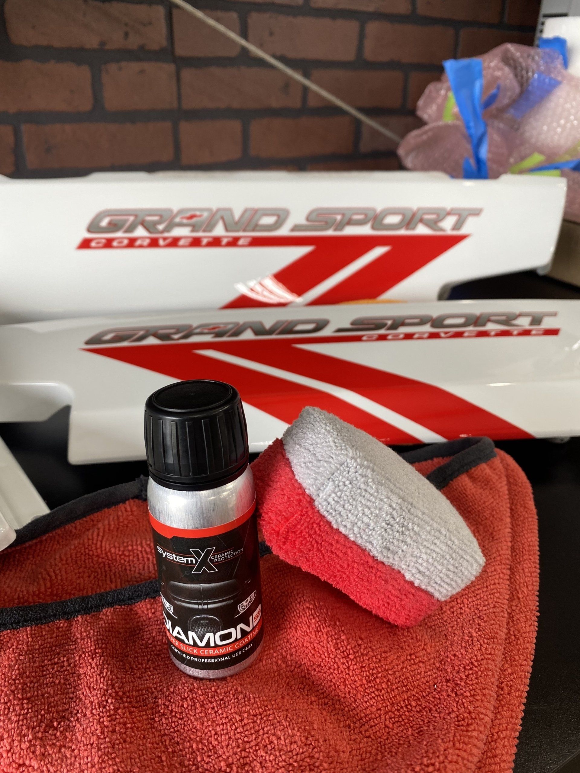 Grand Sport model box with a red-and-white bottle on a red towel, against a brick wall