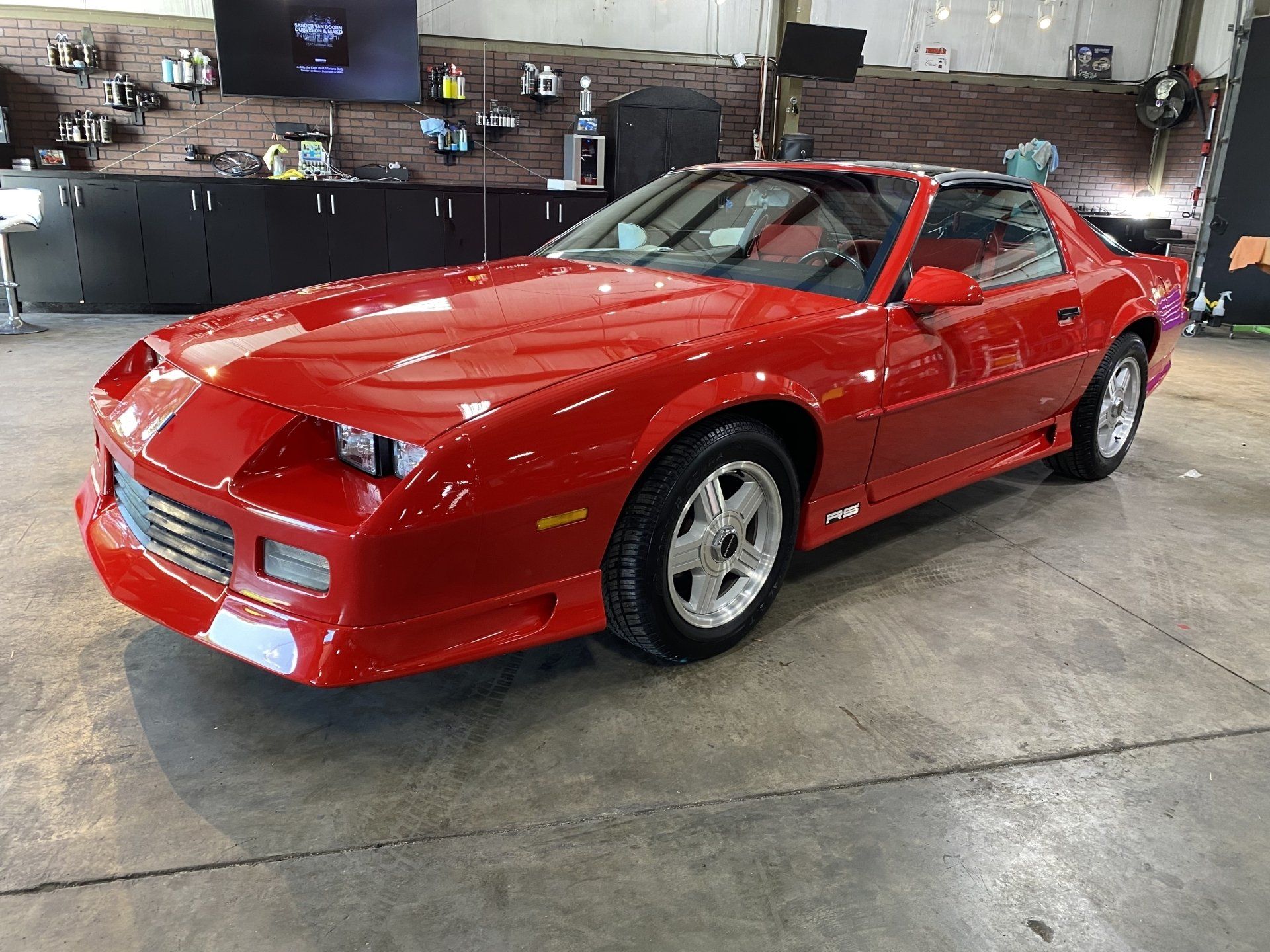 Red sports car in a garage, angled front view with pop-up headlights.