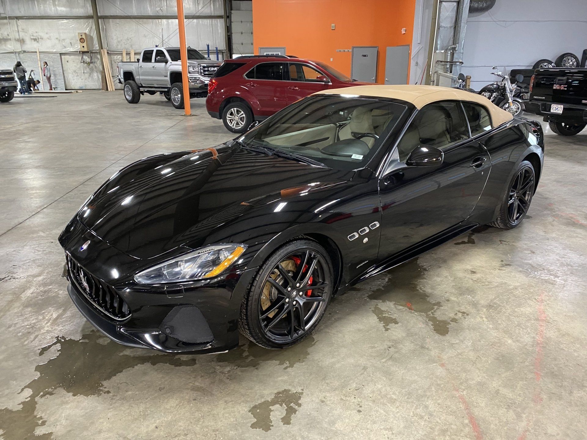 Black sports coupe in a garage, angled front view with beige roof and red brake calipers.