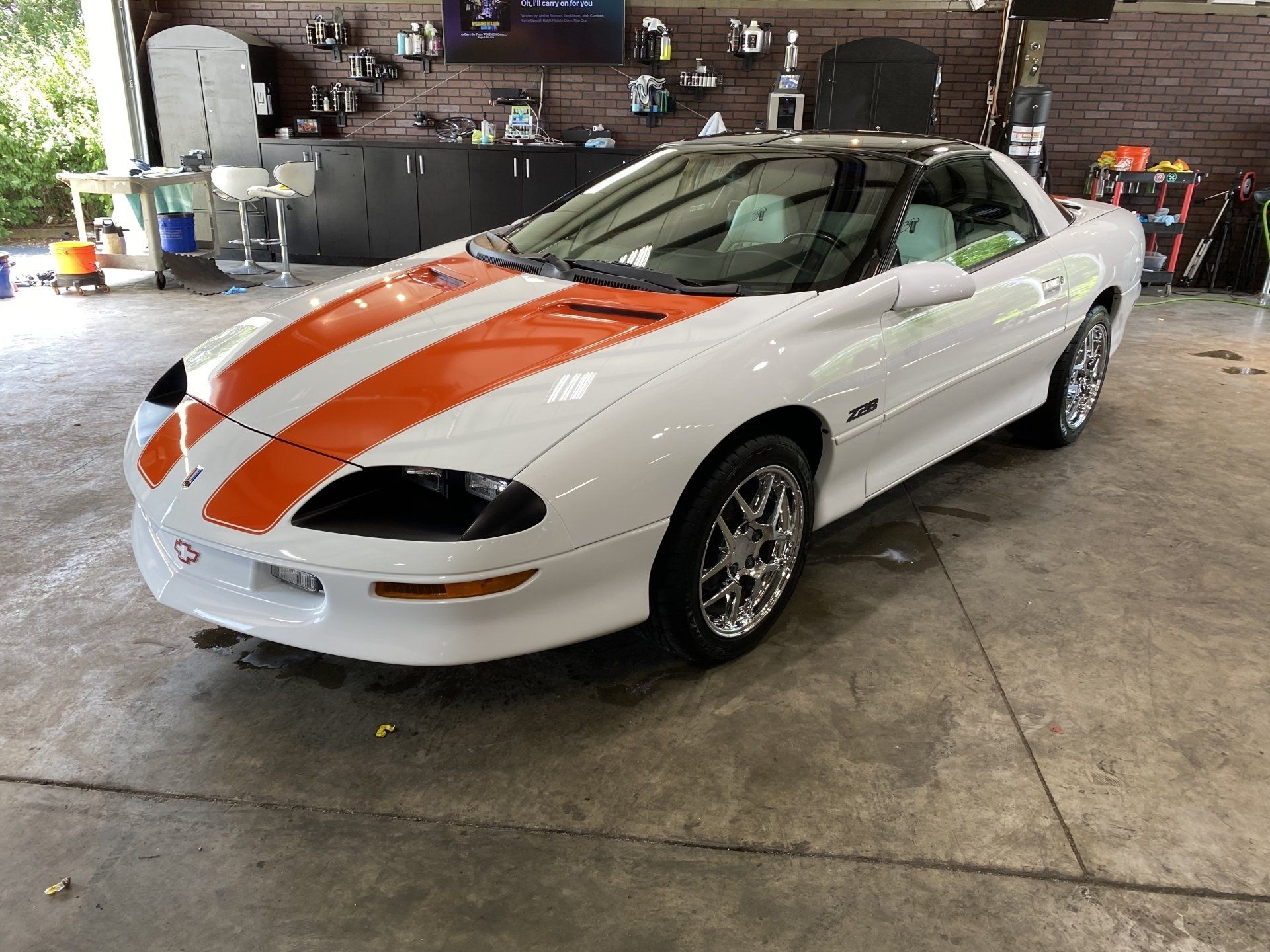 White sports car with orange racing stripes parked indoors in a garage