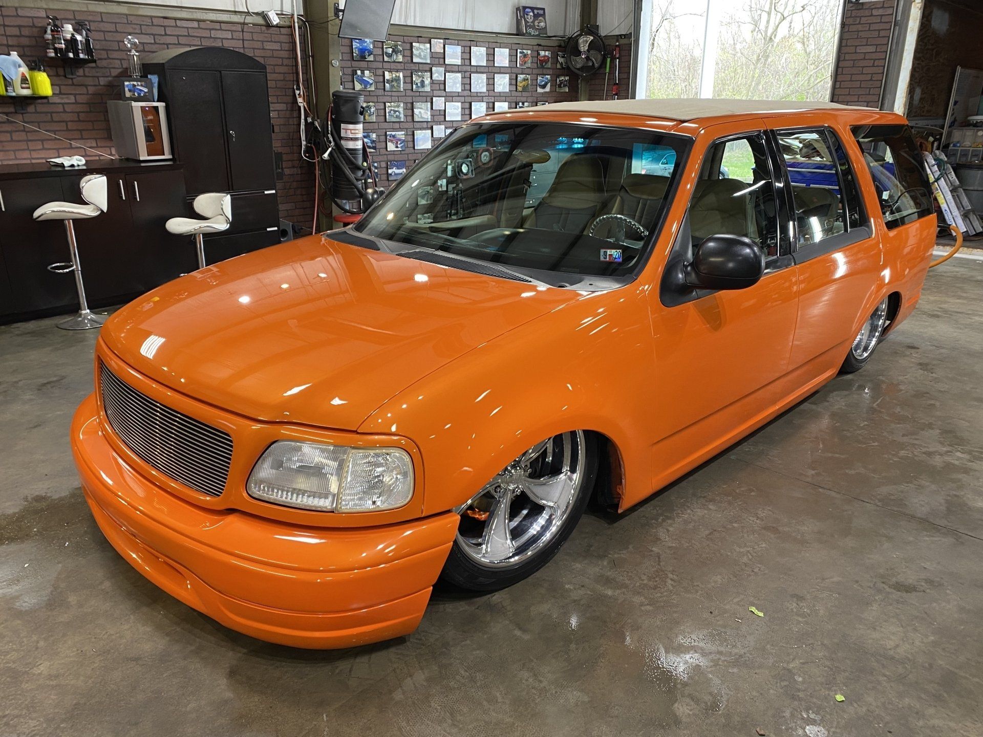 Orange lowered station wagon parked in a garage, with chrome wheels and a custom grille.