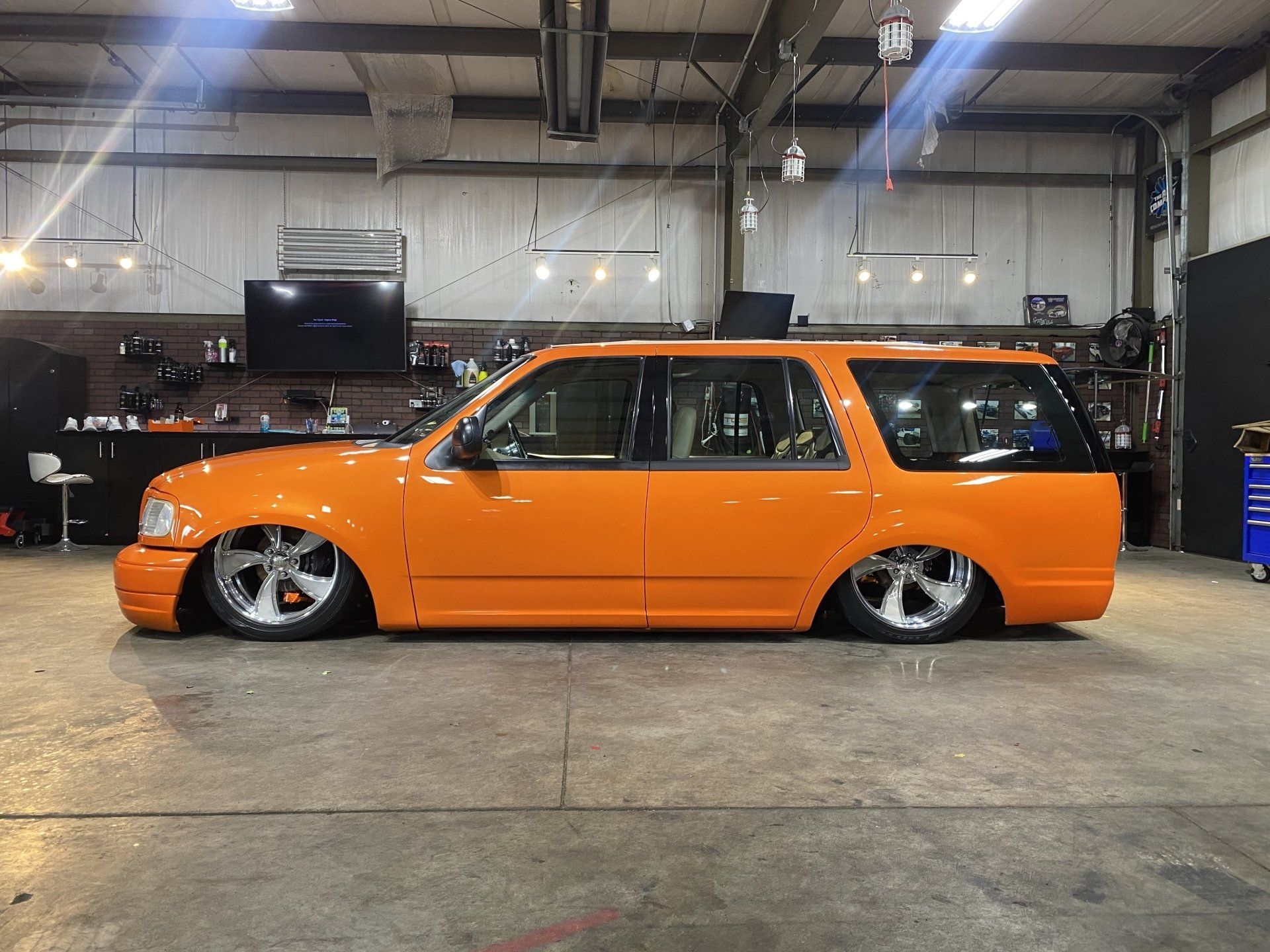 Orange lowered station wagon in a workshop garage with exposed wheels and modified suspension