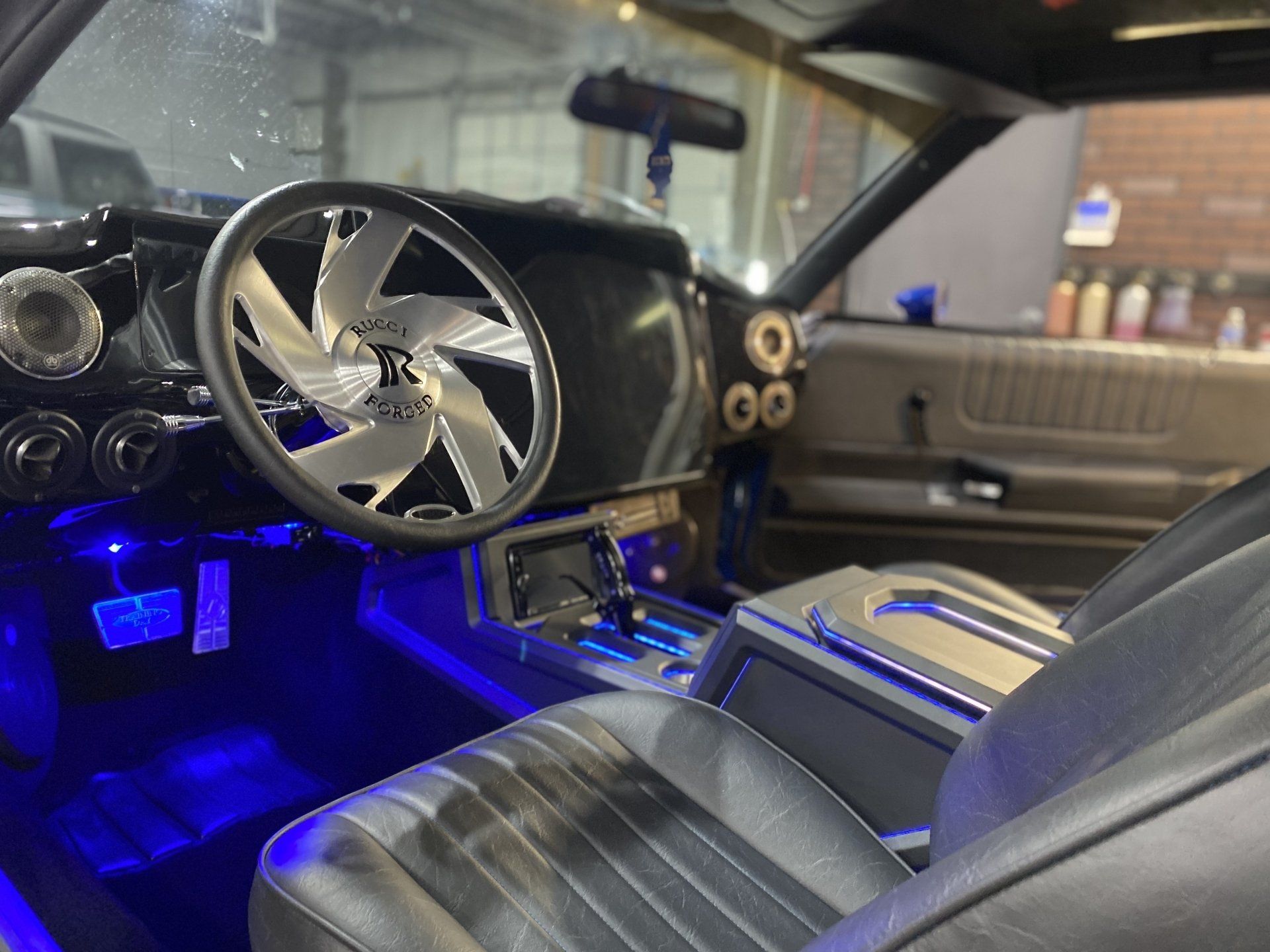 Custom car interior with a chrome steering wheel, black seats, and blue LED lighting.