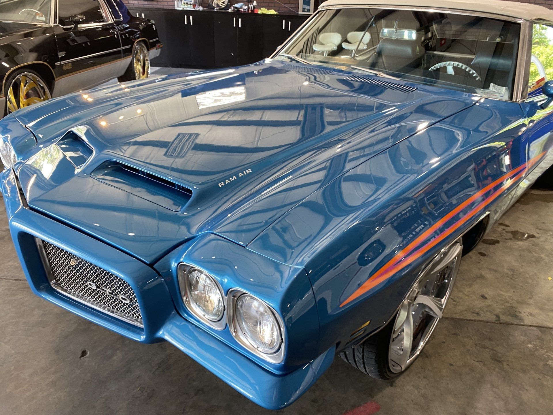 Blue classic car displayed indoors at an auto show, with chrome details and red side stripes
