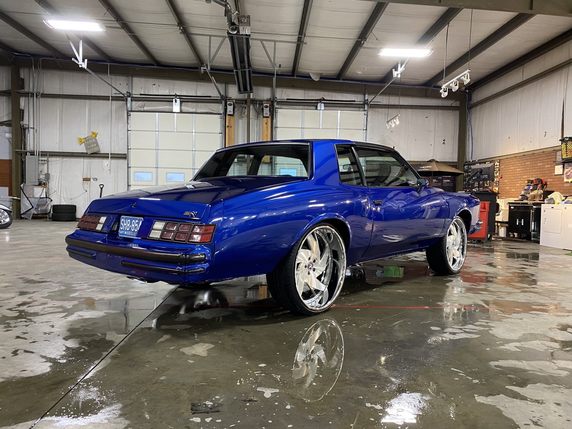 Blue sports coupe in a garage with wet floor and white rims