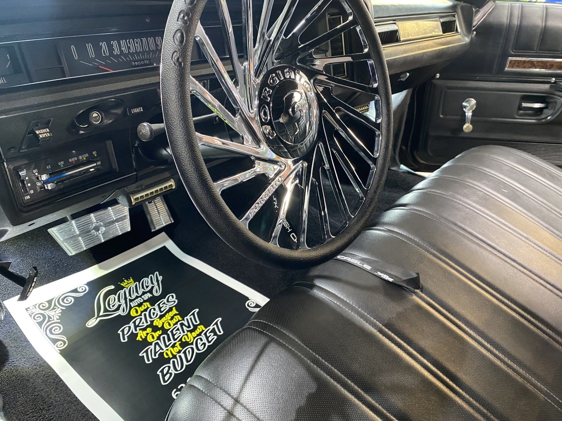 Custom car interior with chrome steering wheel, black leather seat, and logo floor mat