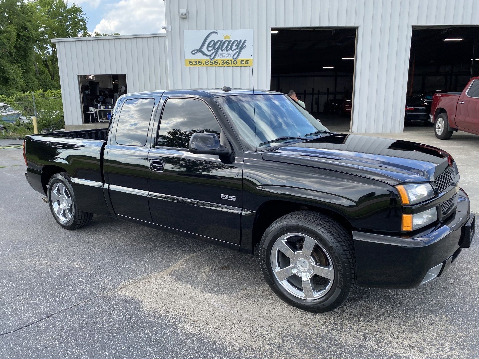 Black extended-cab pickup truck parked outside a dealership garage with a Legacy sign in the background