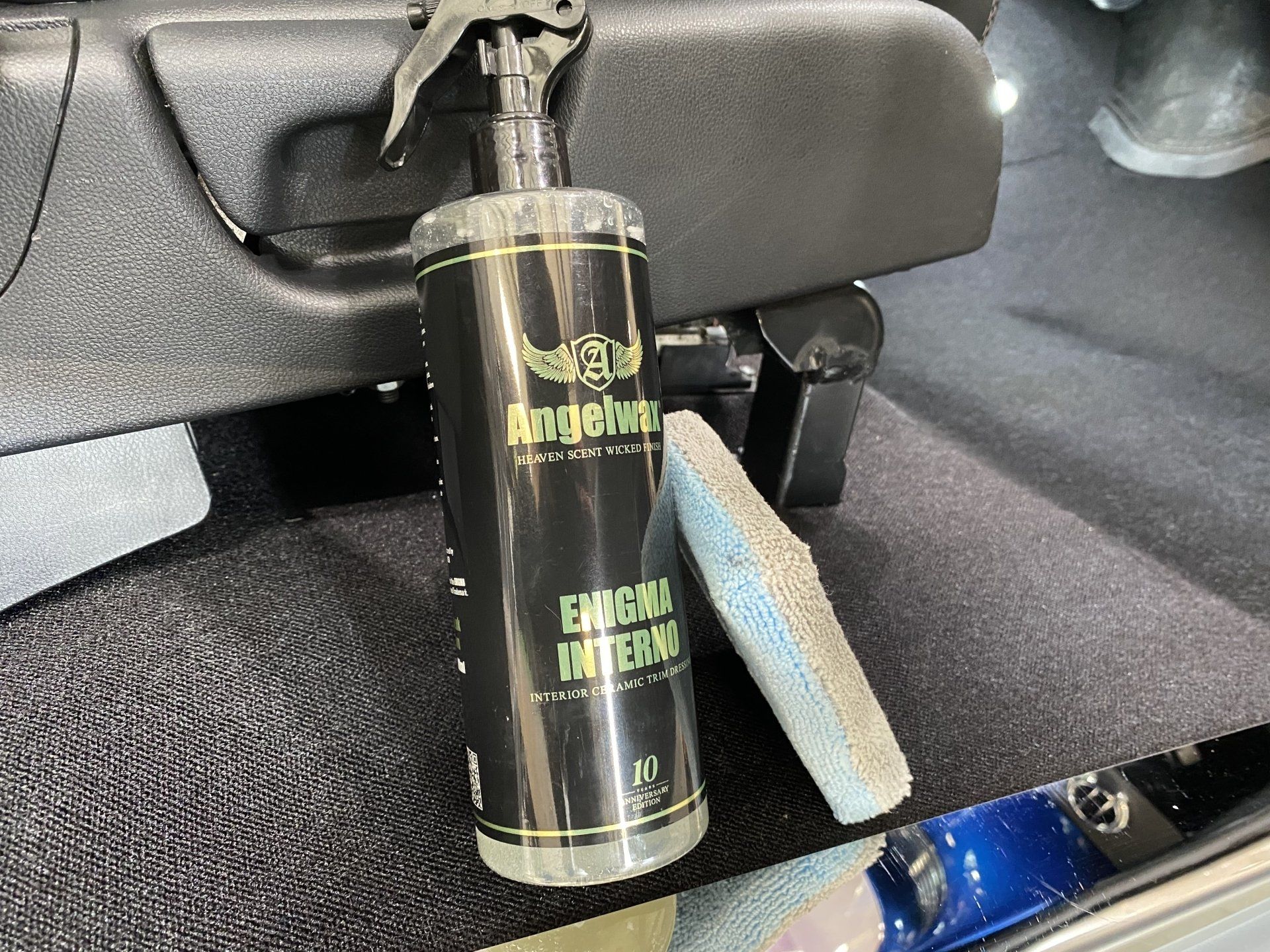 Black bottle strapped under a car dashboard with a blue tag hanging beside it.