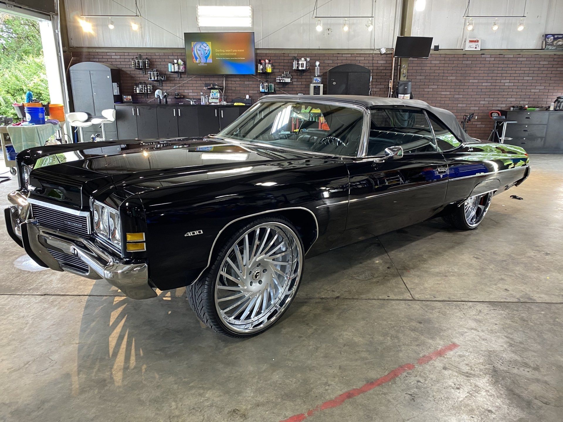 Black classic convertible car with large chrome rims parked indoors in a garage showroom.