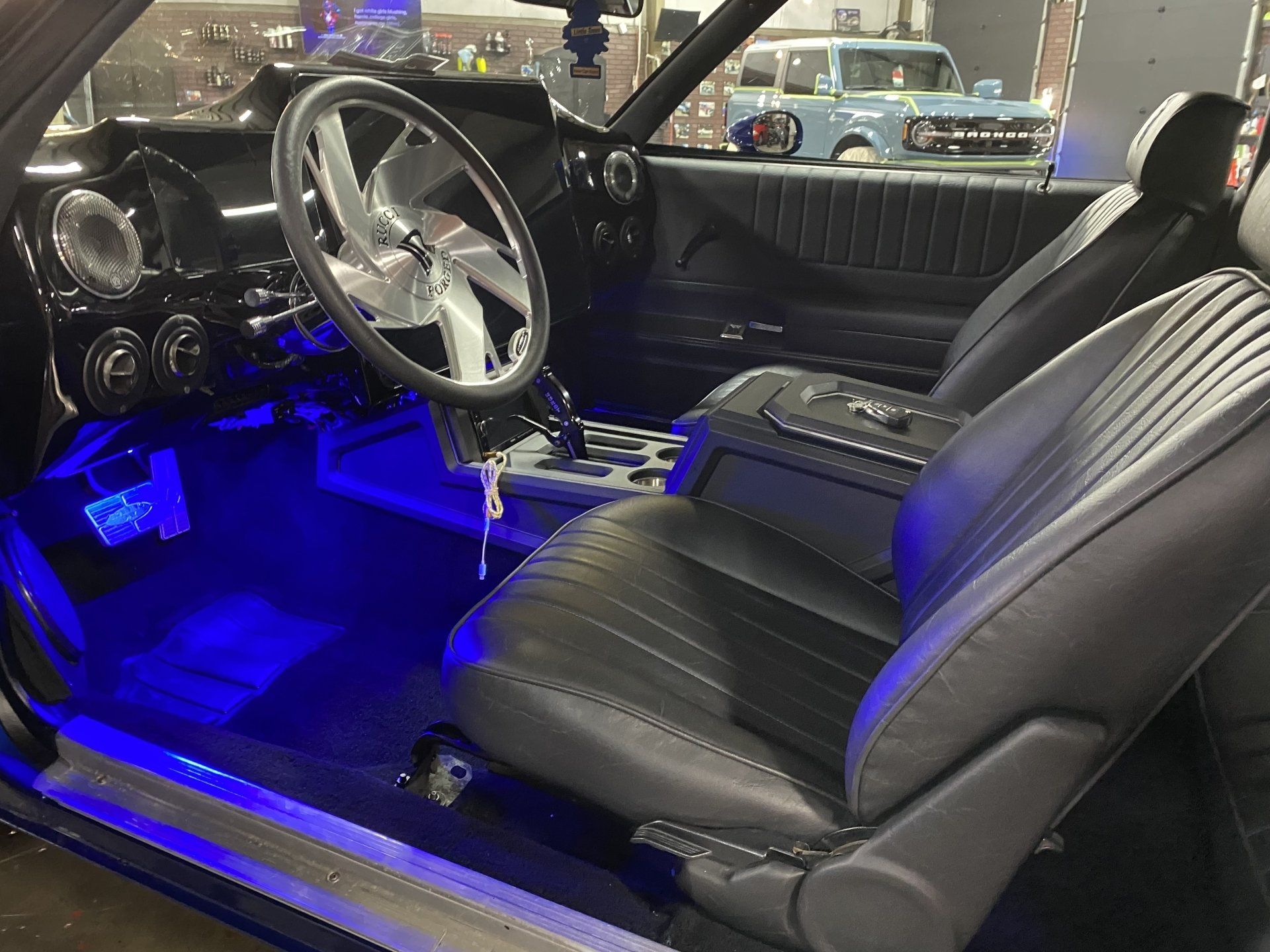 Classic car interior with black leather seats, chrome steering wheel, and blue LED floor lighting