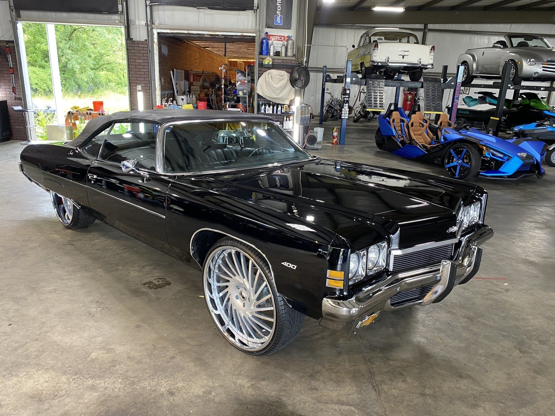 Black classic car with chrome details parked in a garage beside a blue sports car.