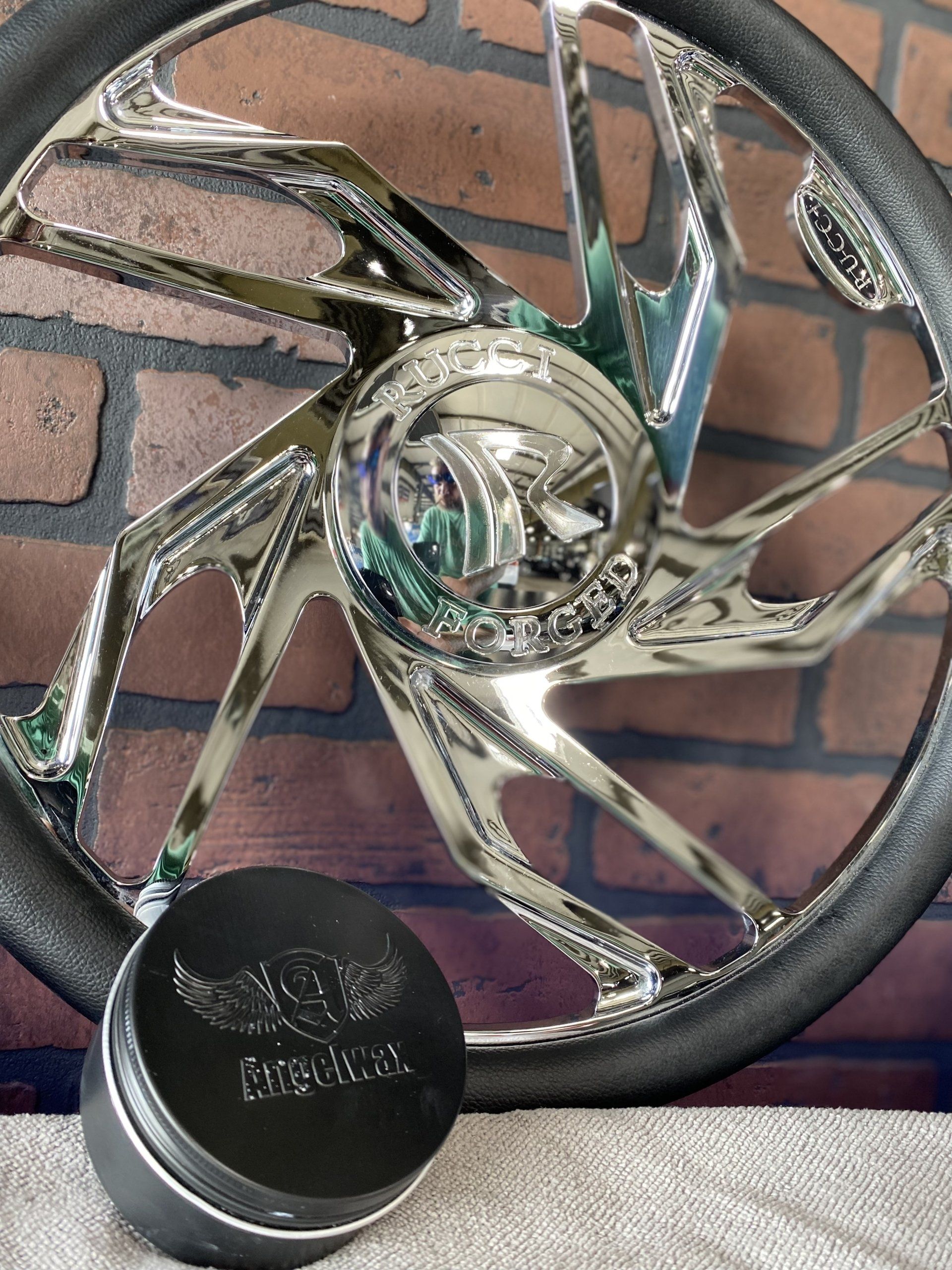 Chrome spiral decorative wheel rim with a black cap resting on a brick surface.